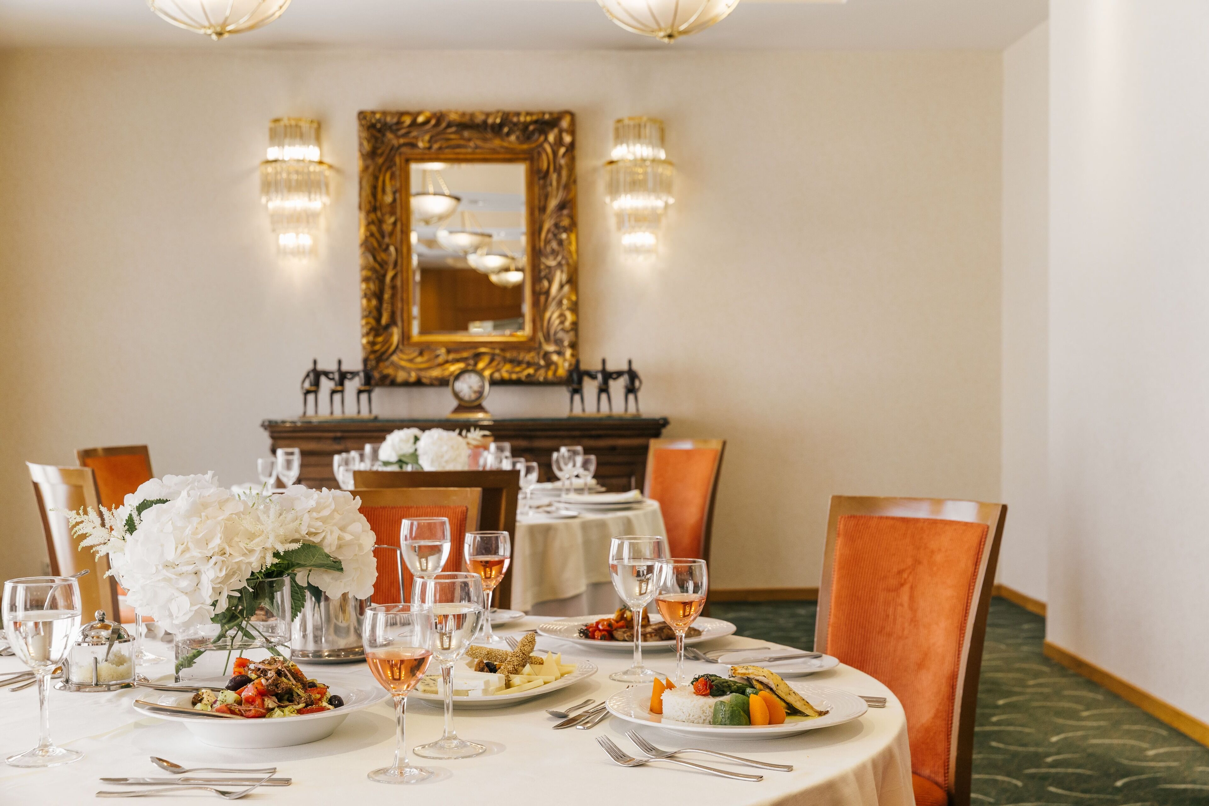 A dining table set with plates of food, wine glasses, and a vase of flowers.