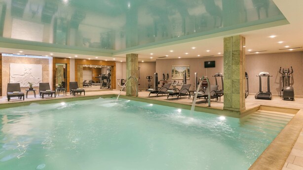 An indoor swimming pool with lounge chairs and exercise equipment. - Divani Palace Larissa (Larissa)