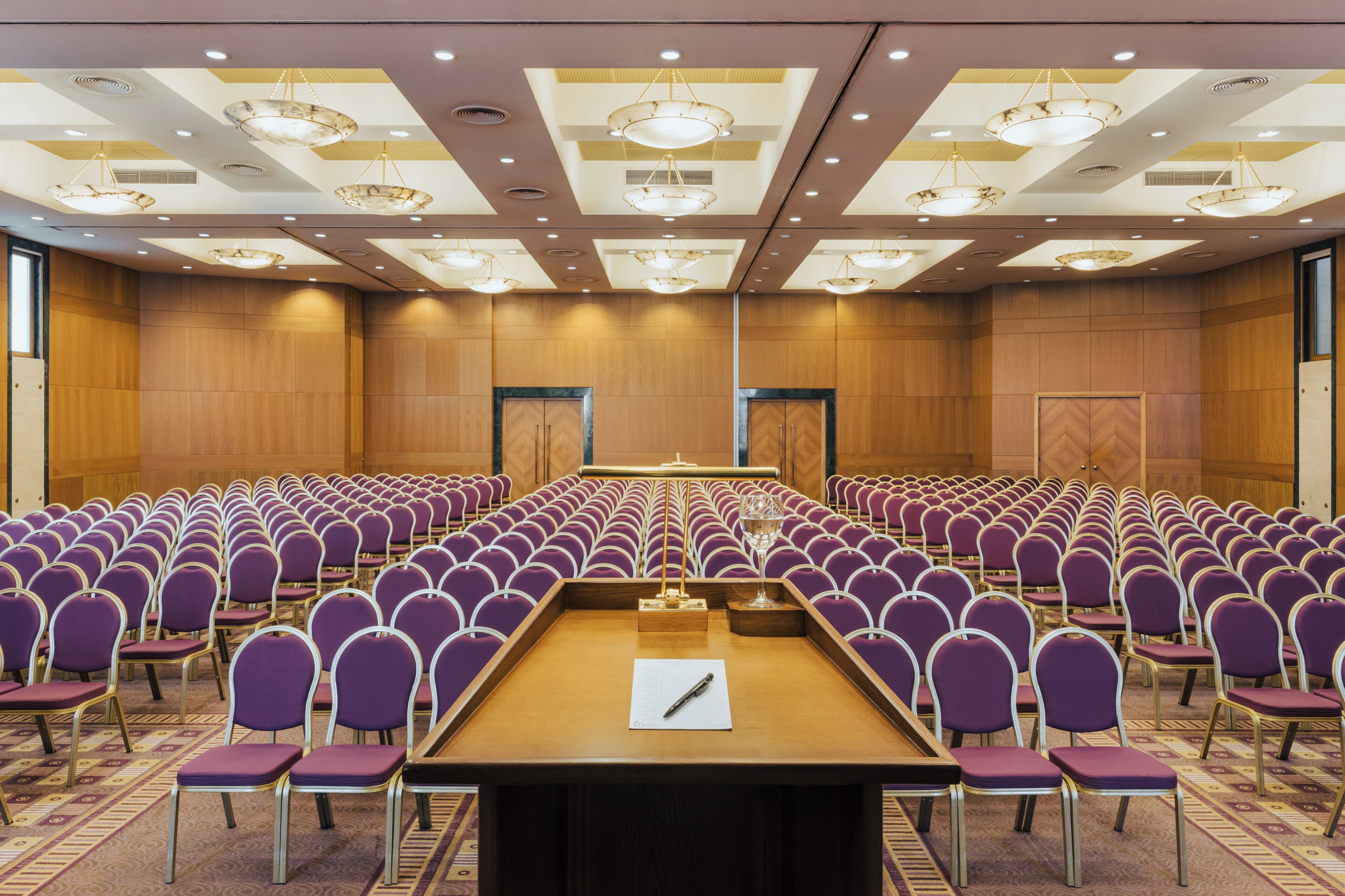 Un salón de conferencias con hileras de sillas moradas, una mesa larga y una gran lámpara de araña.