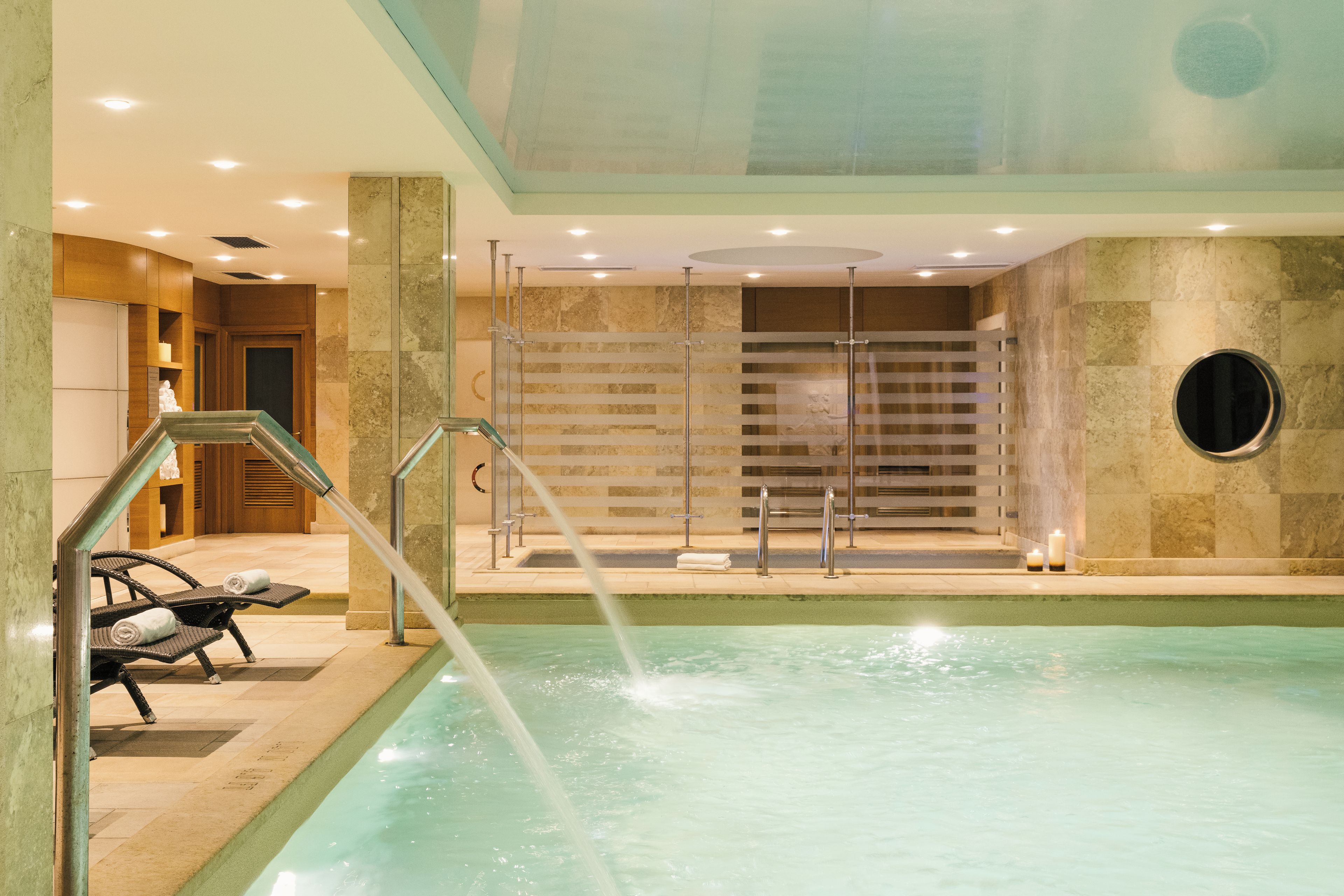 A modern indoor swimming pool with clear water, a glass-enclosed area, and a seating area with a towel.