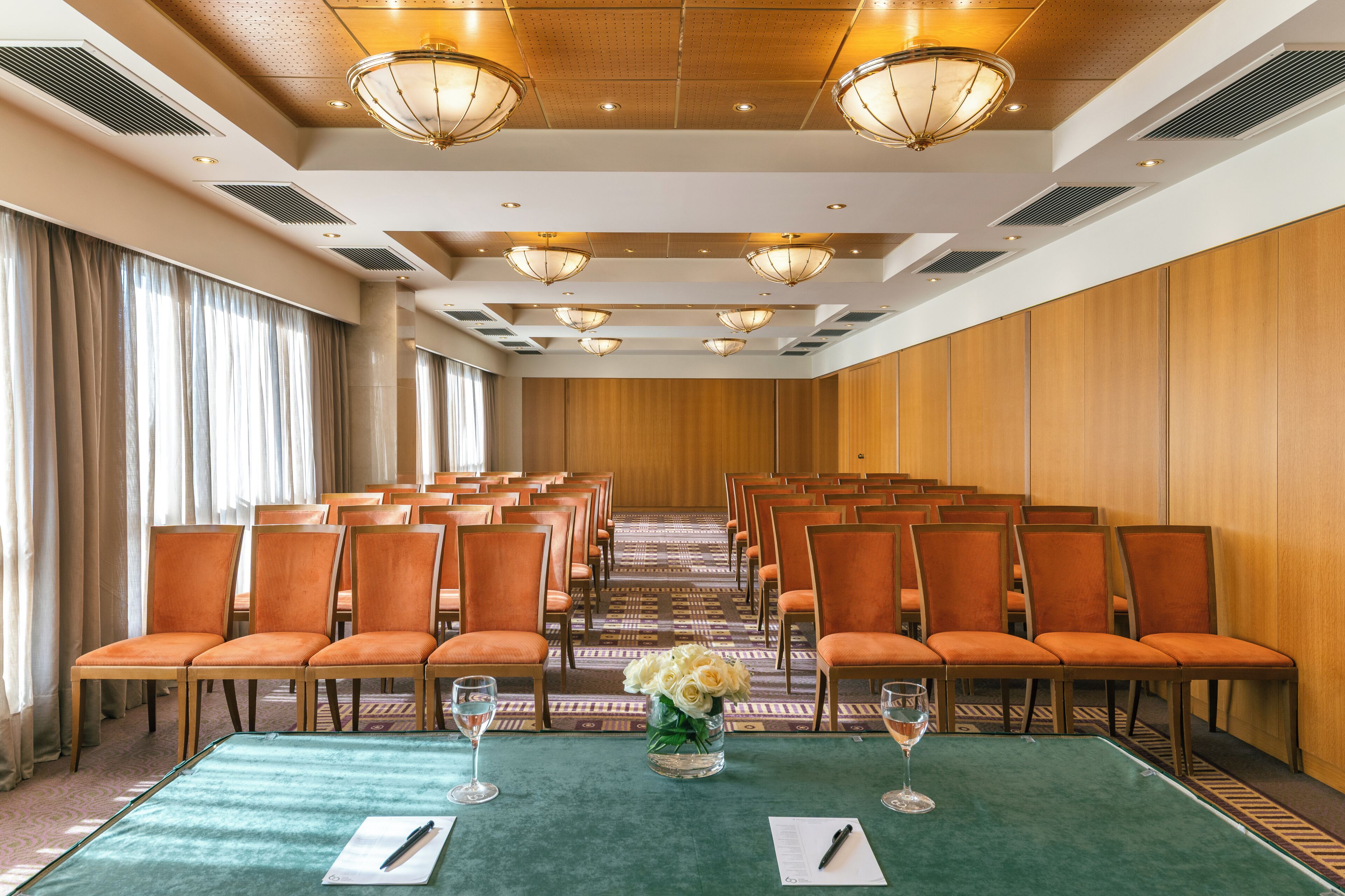 A conference room with rows of chairs, a long table, and a floral centerpiece.