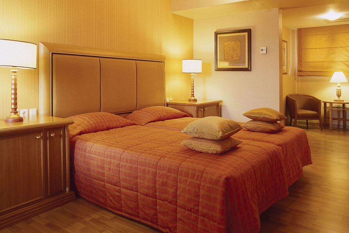 A hotel room with a large bed, bedside tables, a chair, and a lamp.