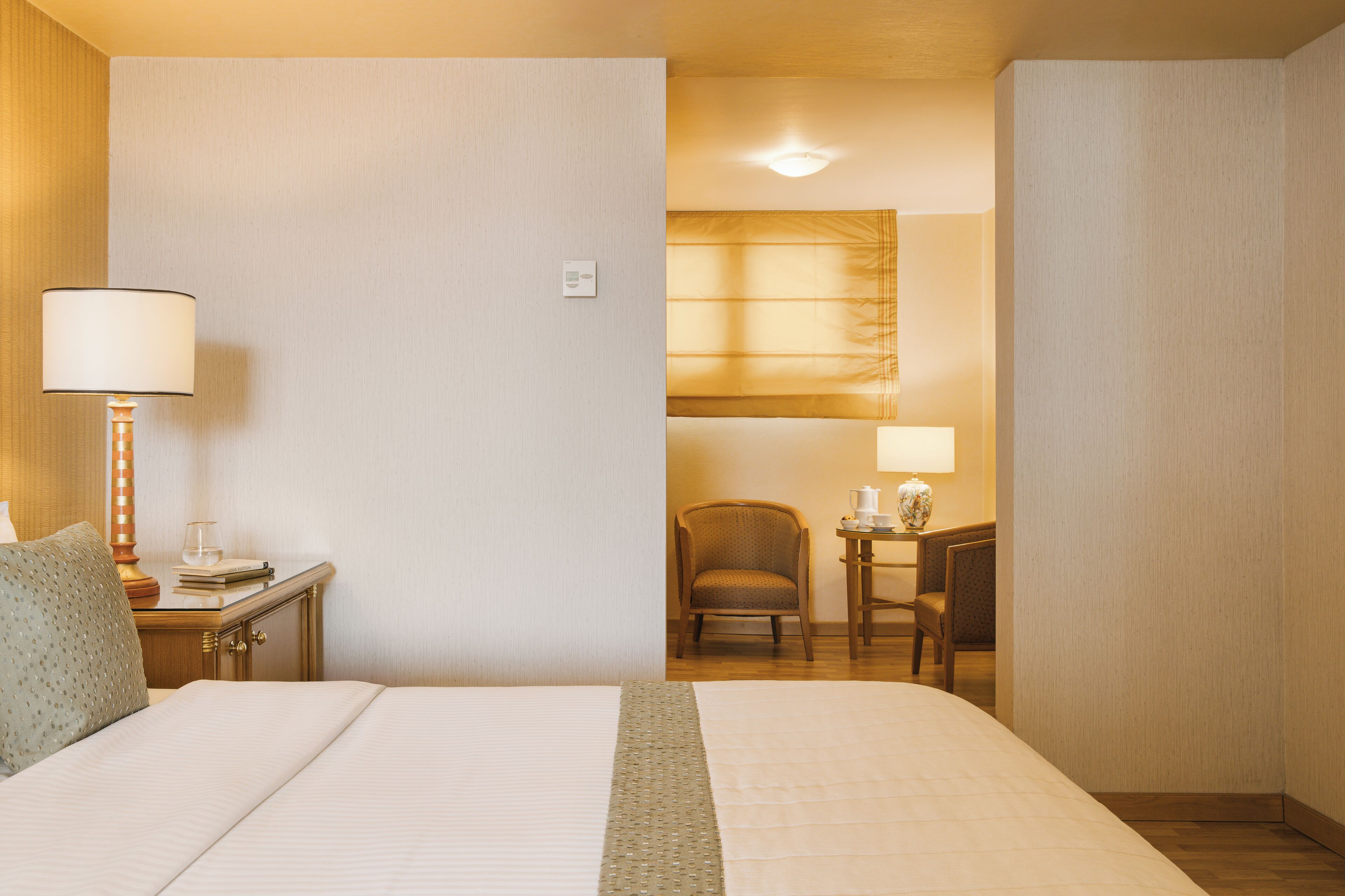 A hotel room with a large bed, a nightstand with a lamp, a chair, and a desk with a lamp.
