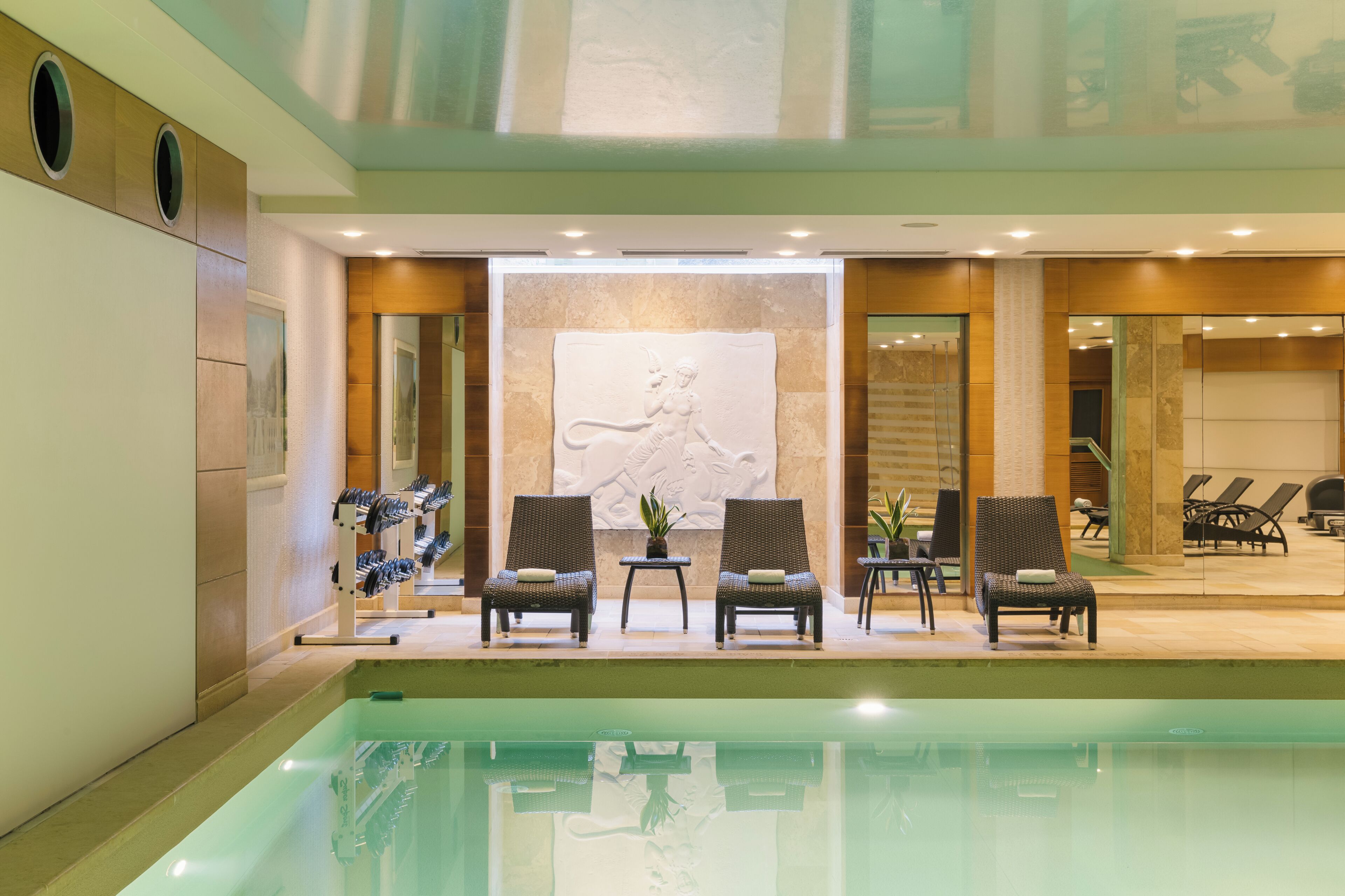 Un espace aménagé au bord de la piscine, avec des chaises longues et une sculpture fixée au mur.