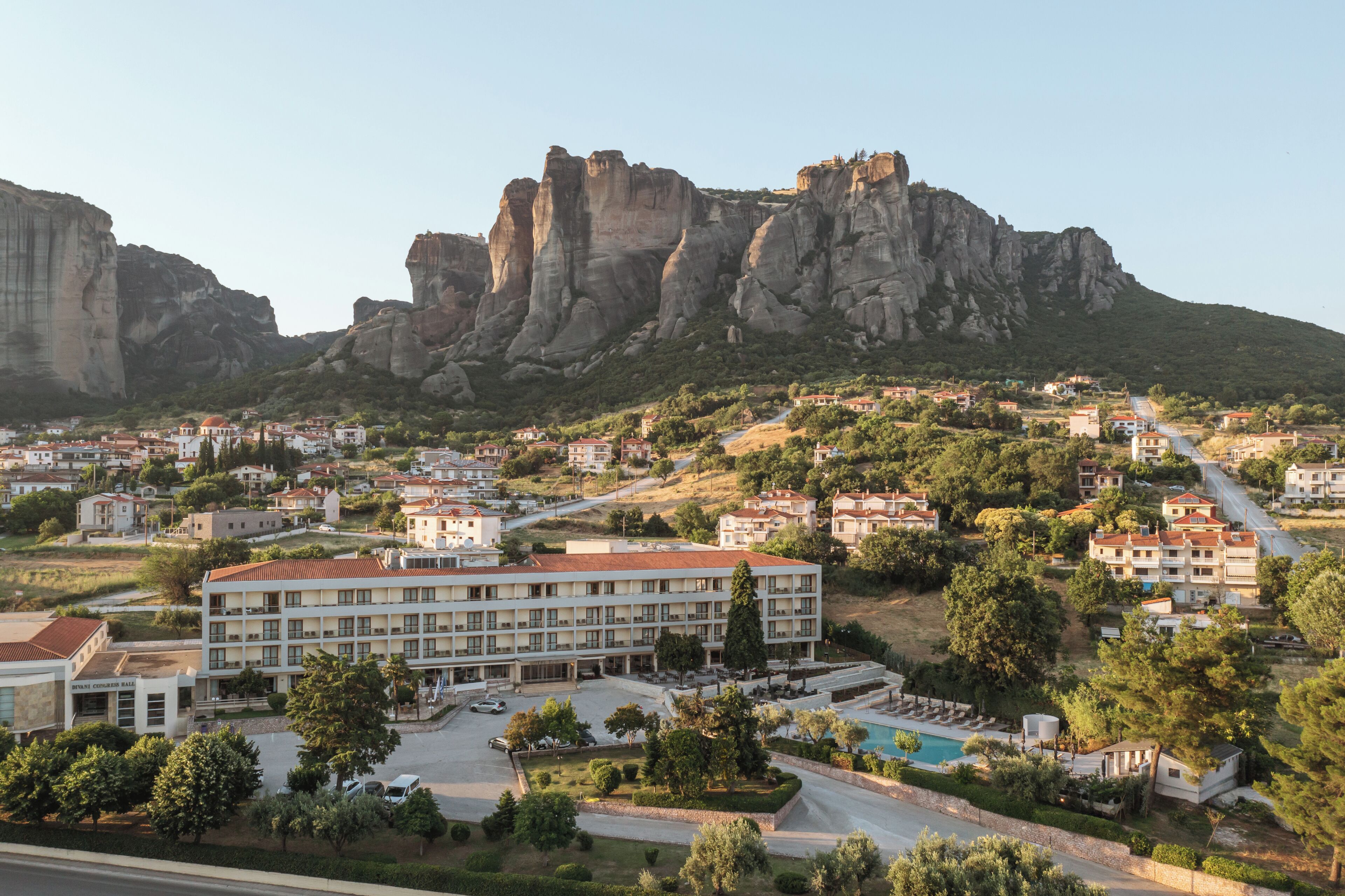 A hotel with a swimming pool, surrounded by greenery and a mountainous backdrop.