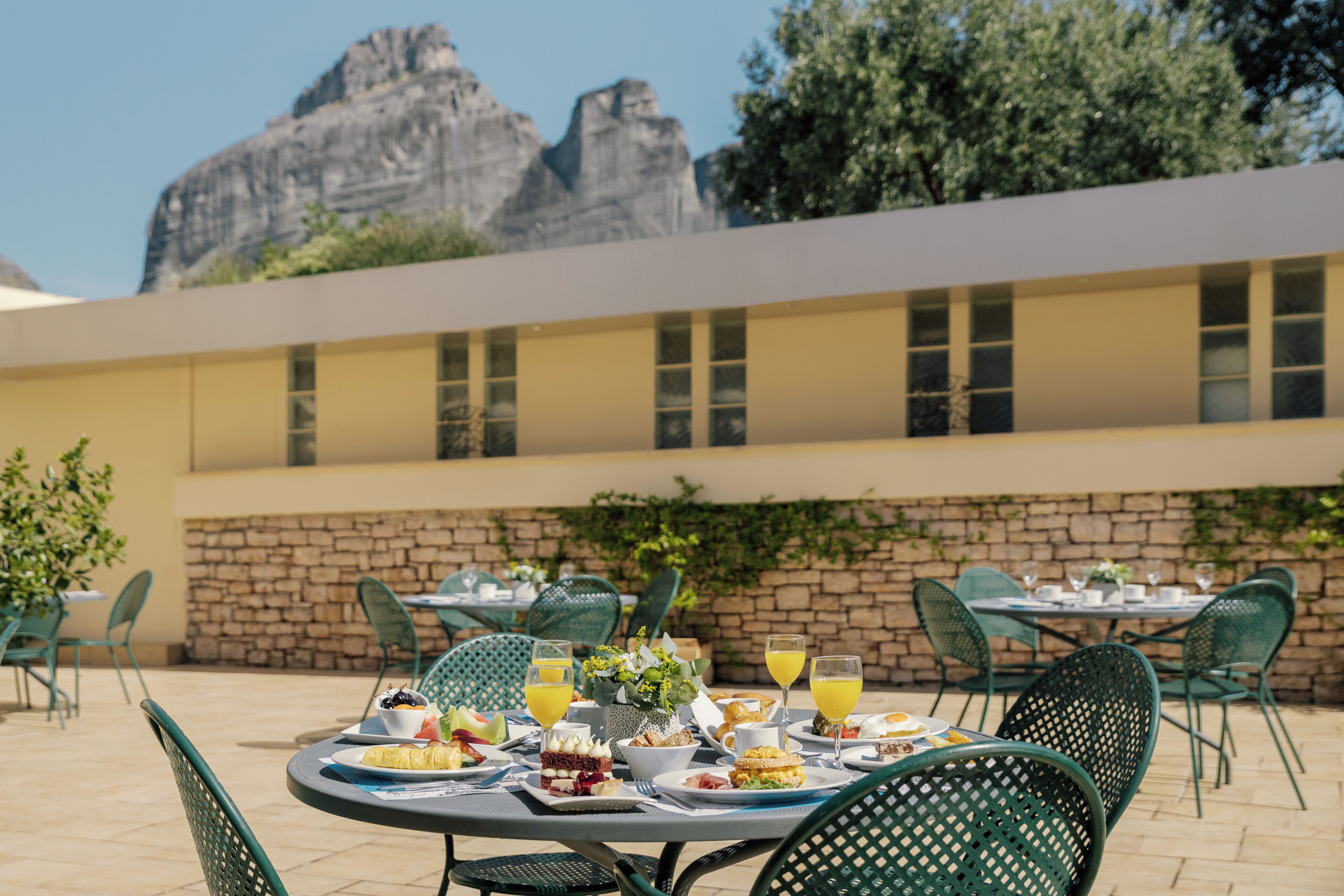 An outdoor dining area with tables set for breakfast, overlooking a mountainous landscape.