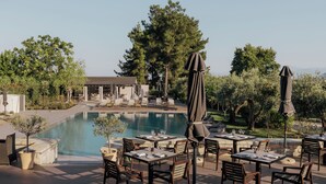 An outdoor dining area with tables and chairs, a pool, and a view of the surrounding landscape.