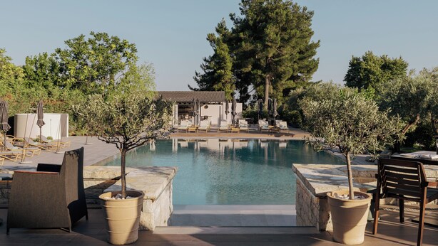 A pool area with lounge chairs, a bar, and a view of a building in the background.
