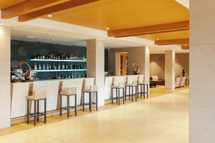 Zona de bar con una barra alargada, varios taburetes y estantes llenos de botellas.