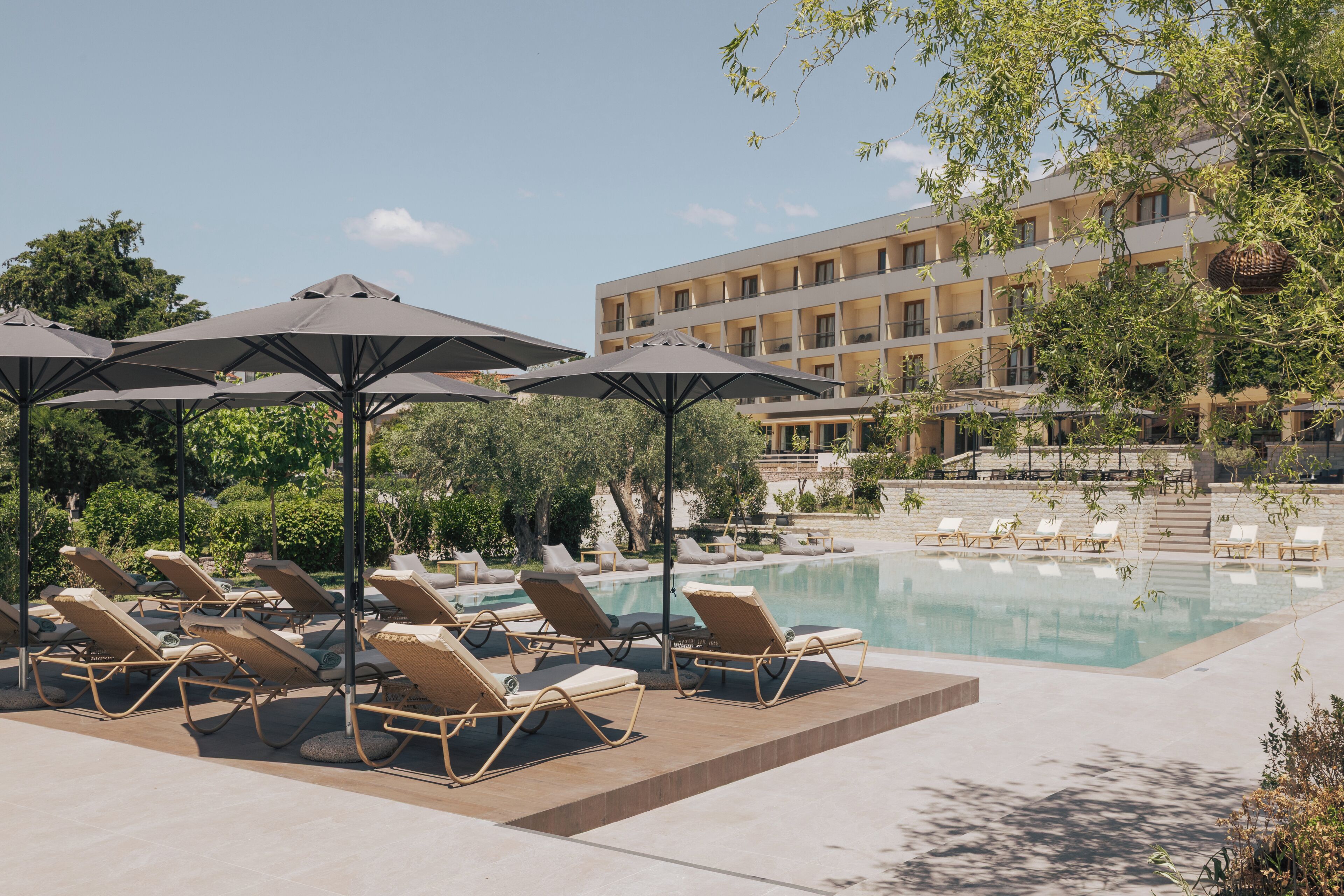 A poolside area with lounge chairs and umbrellas, a clear sky, and a building in the background.