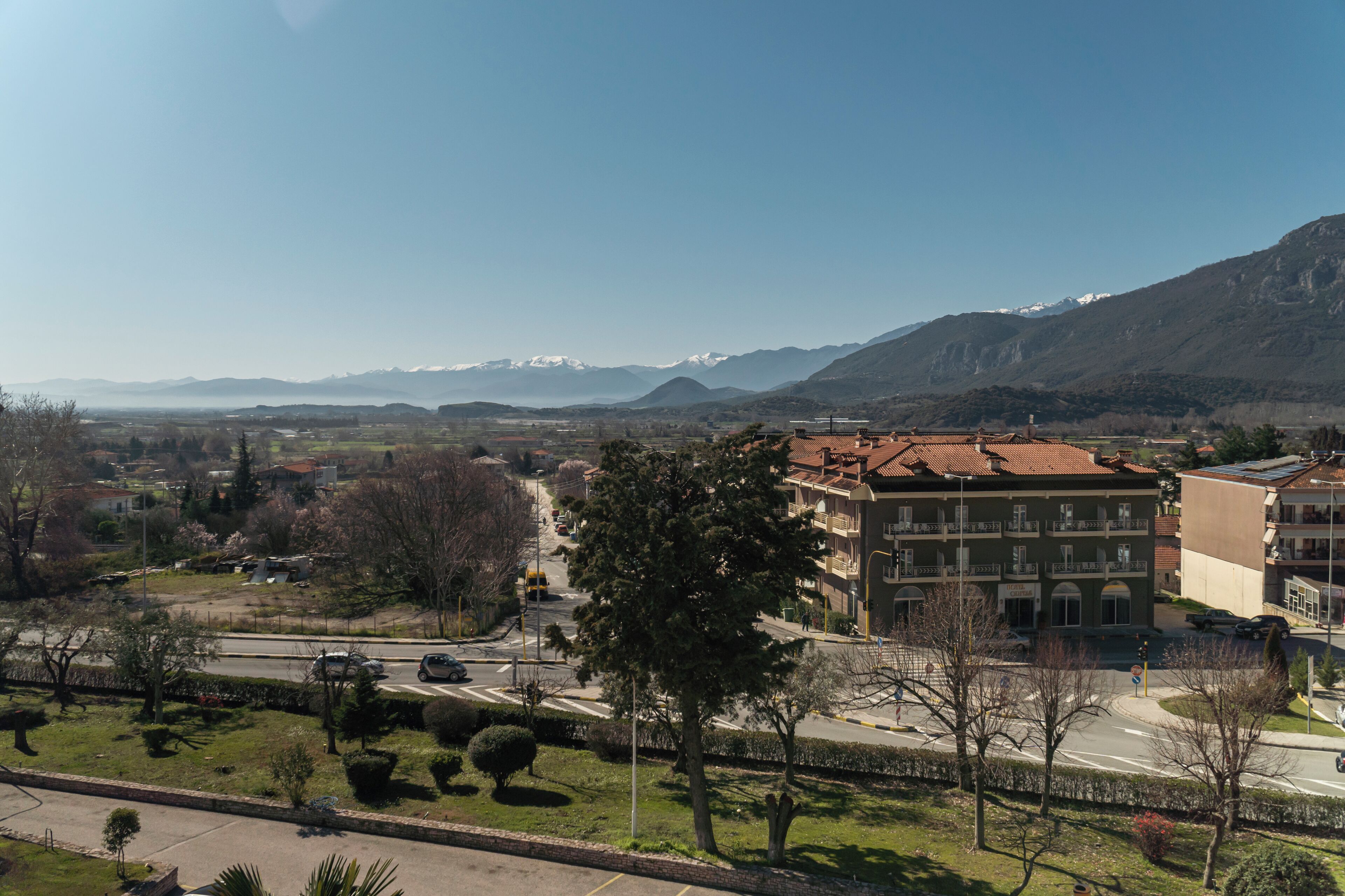 Un barrio residencial con un edificio destacado que tiene techo de tejas rojas, rodeado de vegetación y una vista despejada de montañas lejanas.
