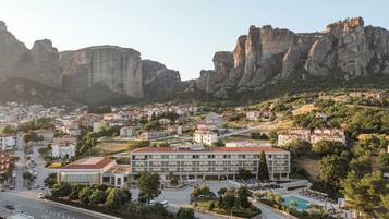 A hotel with a swimming pool, surrounded by greenery and a mountainous backdrop.