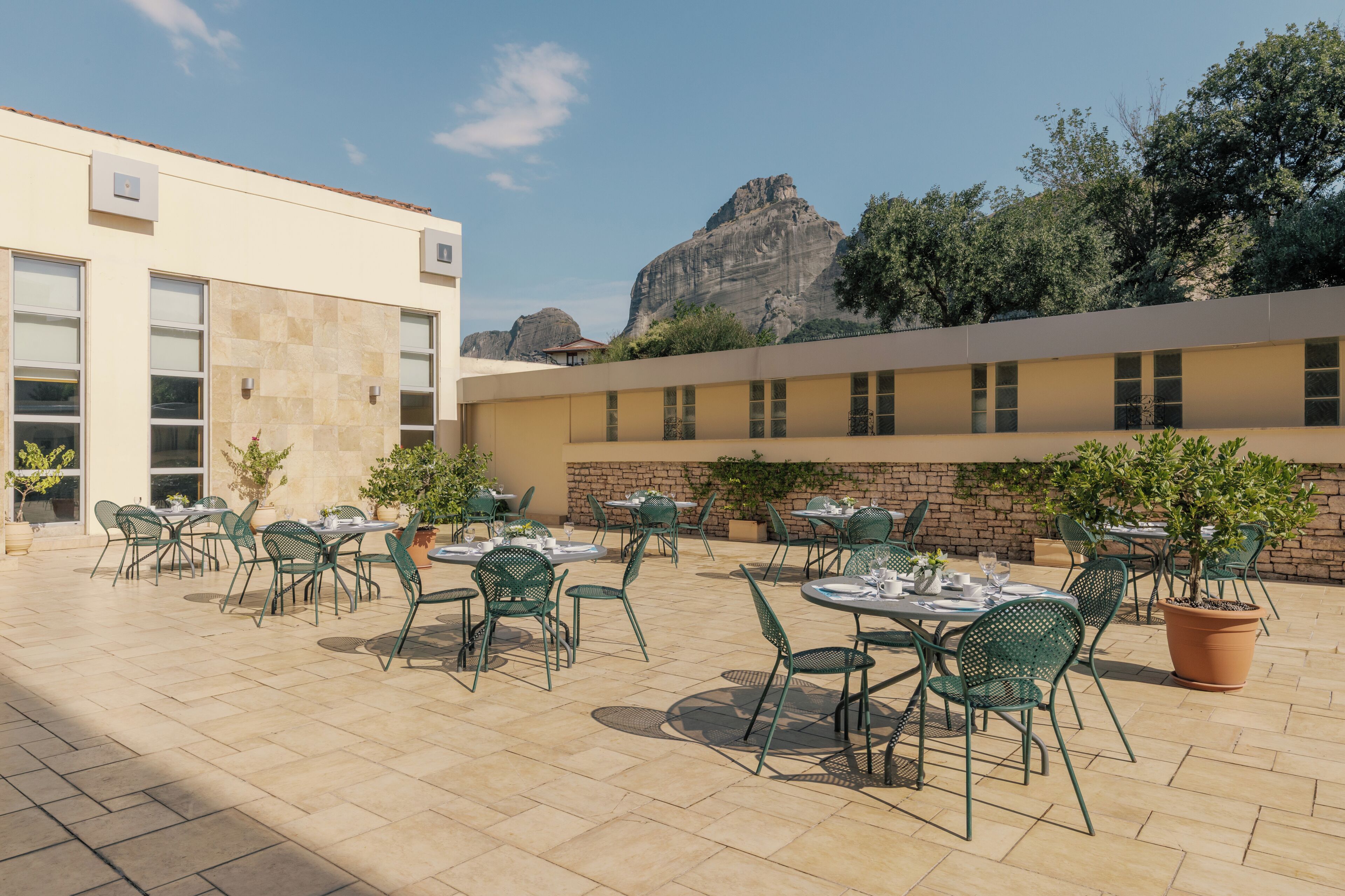 An outdoor patio with tables and chairs, a building with large windows, and a mountain in the background.