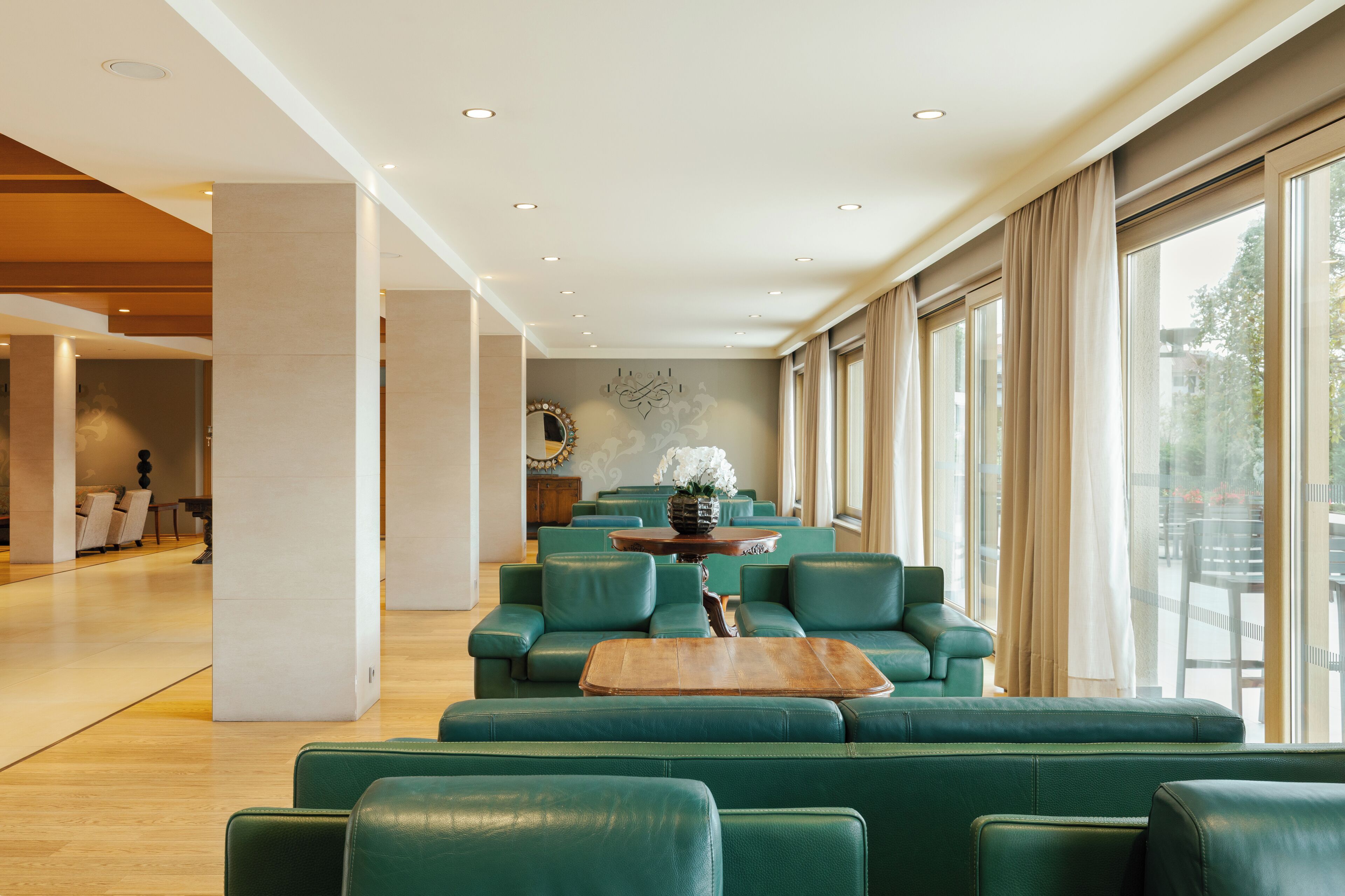 A spacious lobby with green leather seating, a wooden coffee table, and large windows with curtains.