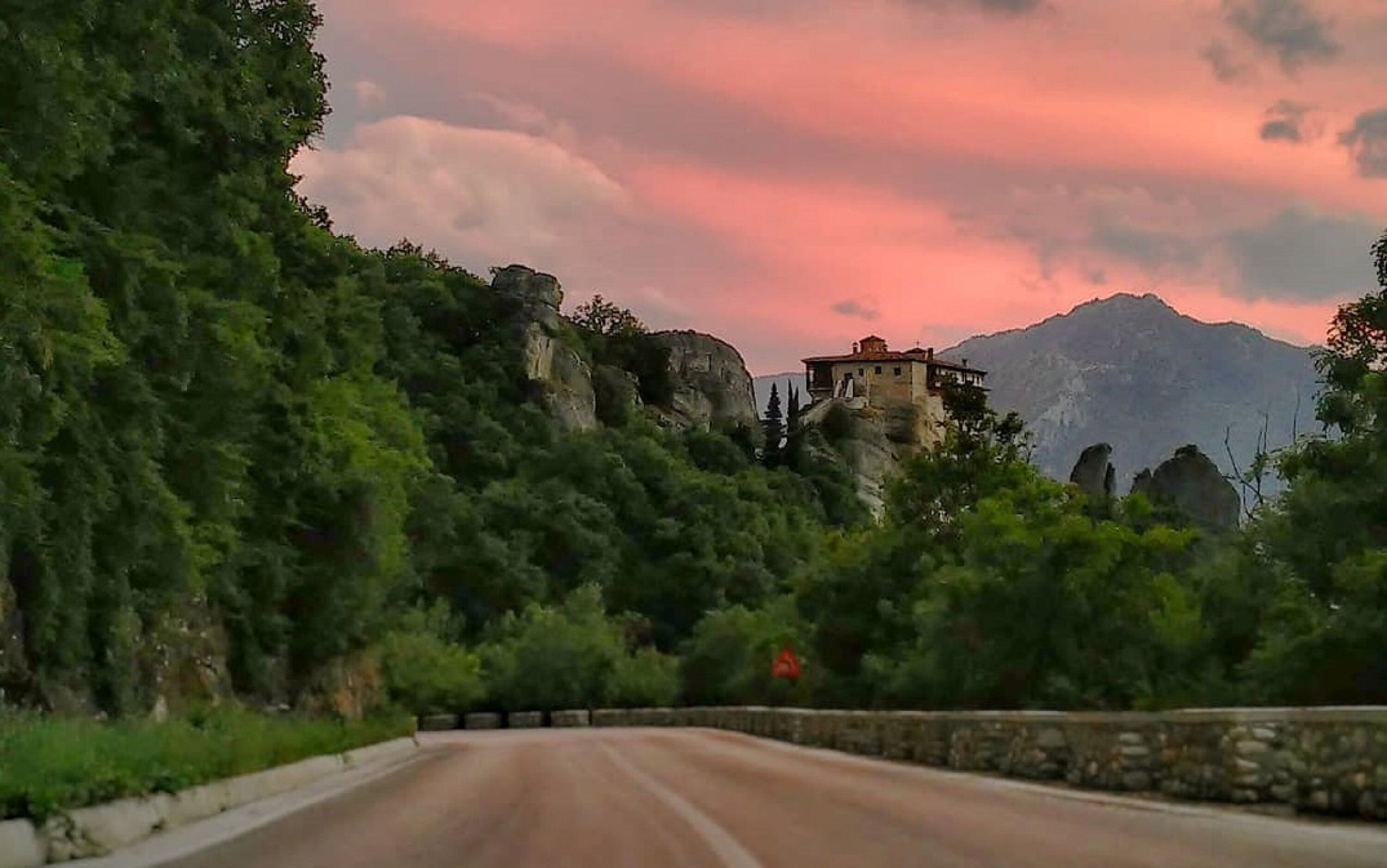 A road leading to a building on a hill with a stone wall on one side.
