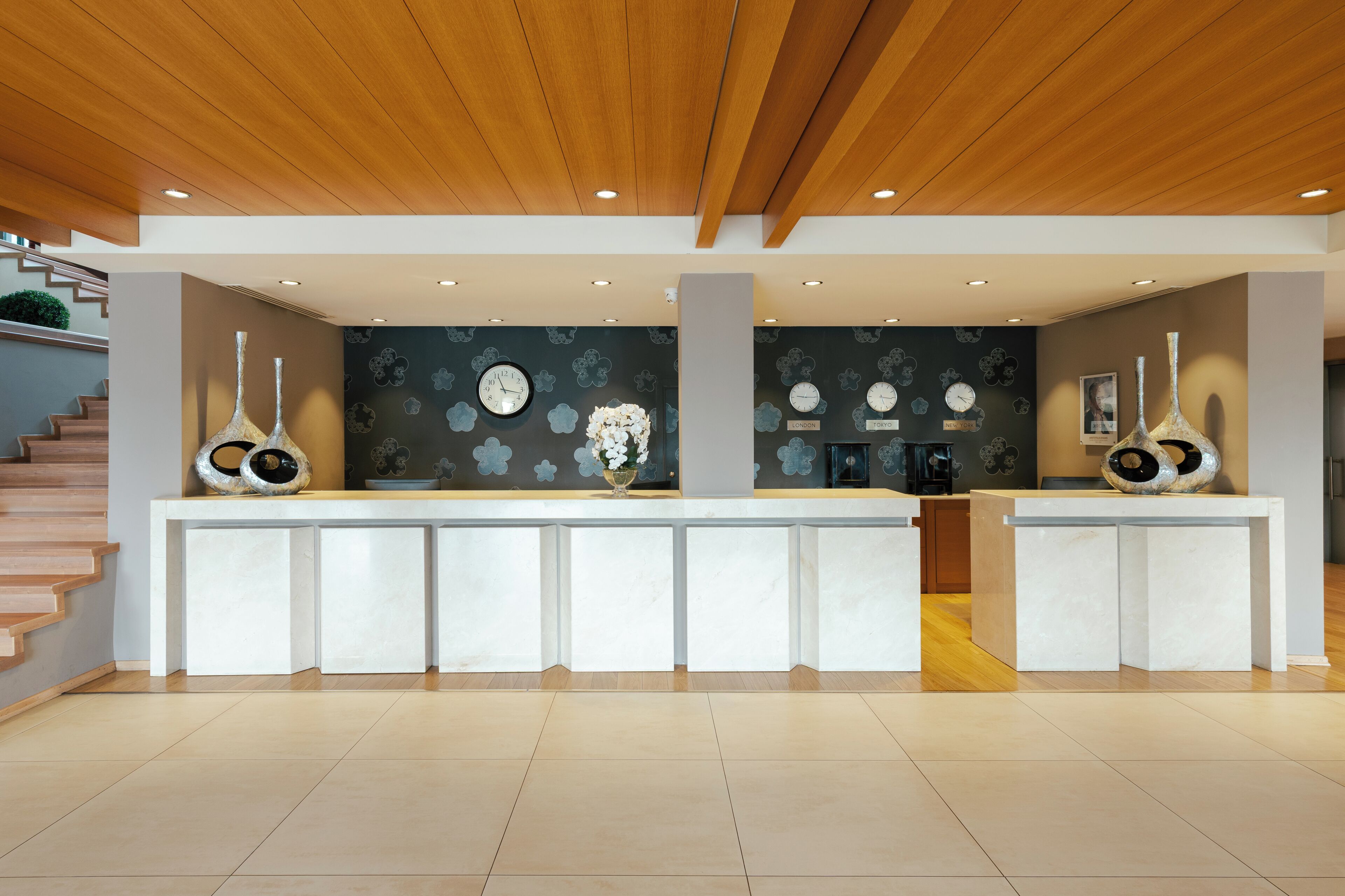 A reception area with a wooden ceiling, a reception desk, a clock, and a wall with city names.
