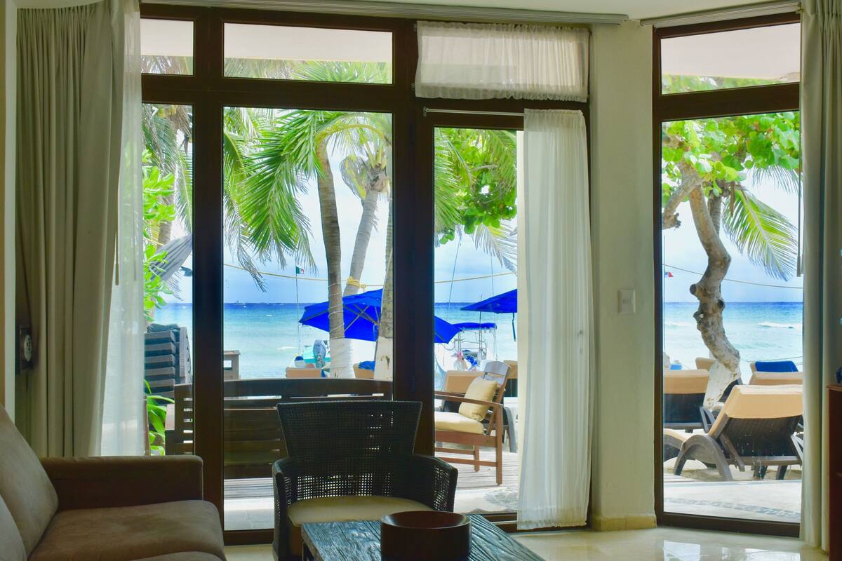 Ein Zimmer mit Blick auf den Strand, ausgestattet mit einer Couch, einem Korbsessel und einem Tisch.
