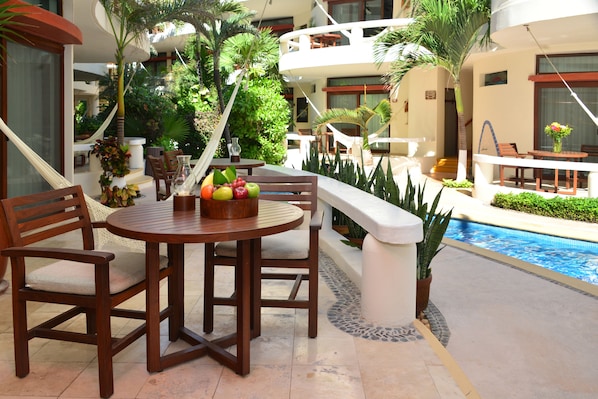 A poolside area with a round wooden table and chairs, surrounded by lush greenery and a swimming pool. - Playa Palms Beach Hotel (Playa del Carmen)