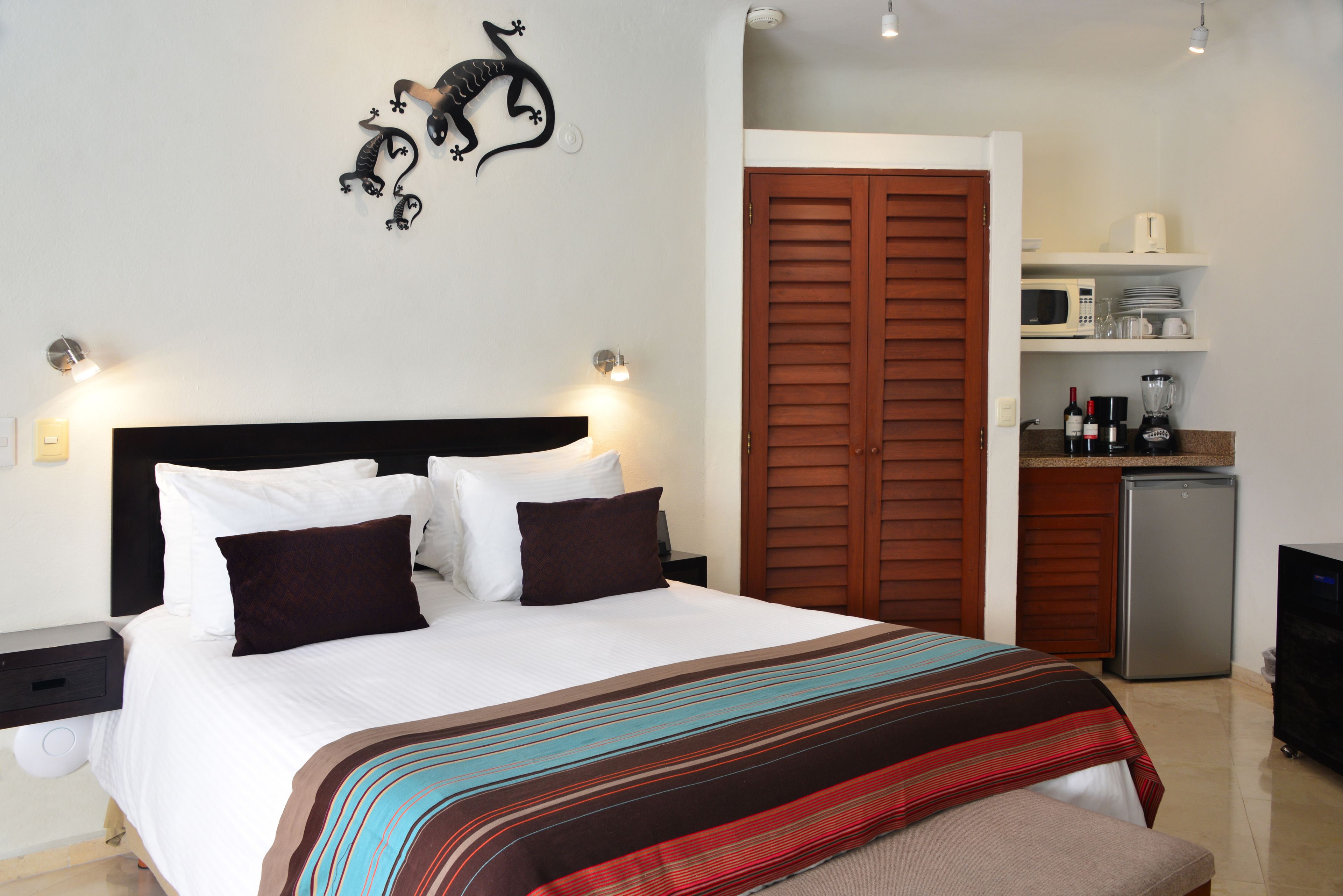 Un lit bien fait, recouvert d’une couverture à rayures, un élément décoratif fixé au mur et un coin cuisine équipé d’appareils électroménagers.