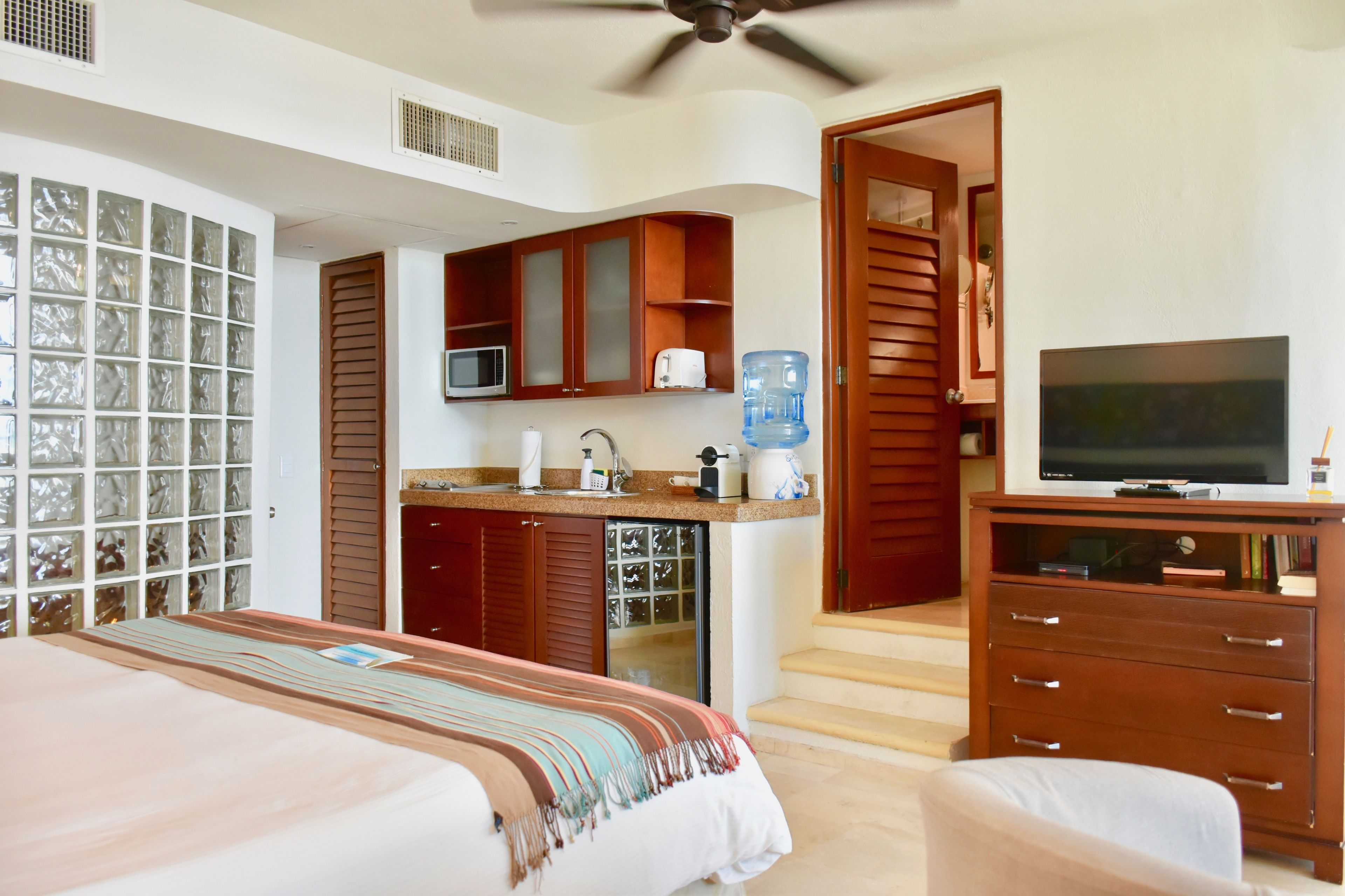 A hotel room with a bed, a TV, a kitchenette, and a bathroom.