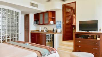 A hotel room with a bed, a TV, a kitchenette, and a bathroom.