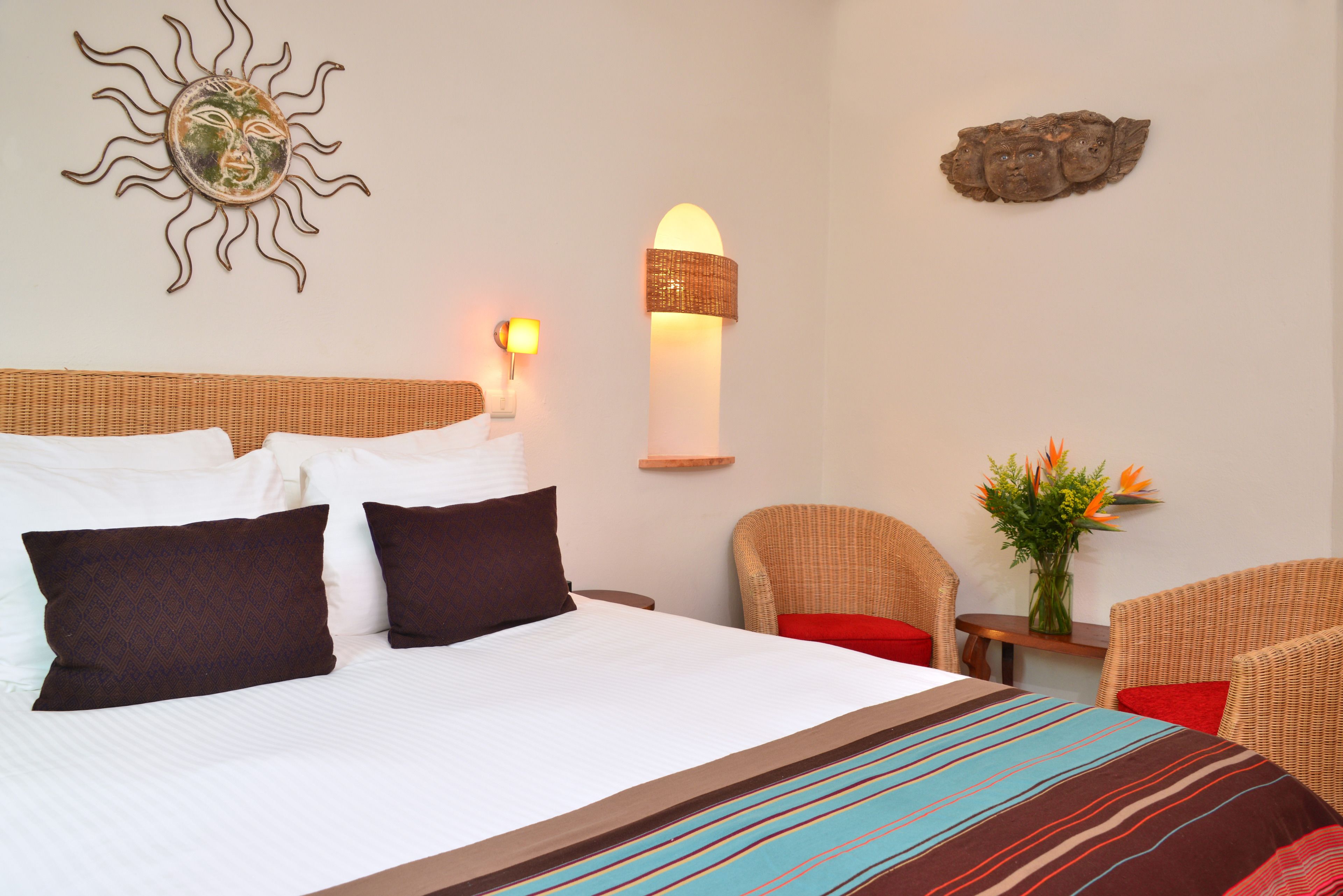 Une chambre d’hôtel avec un grand lit, deux chaises, une petite table et une lampe fixée au mur.
