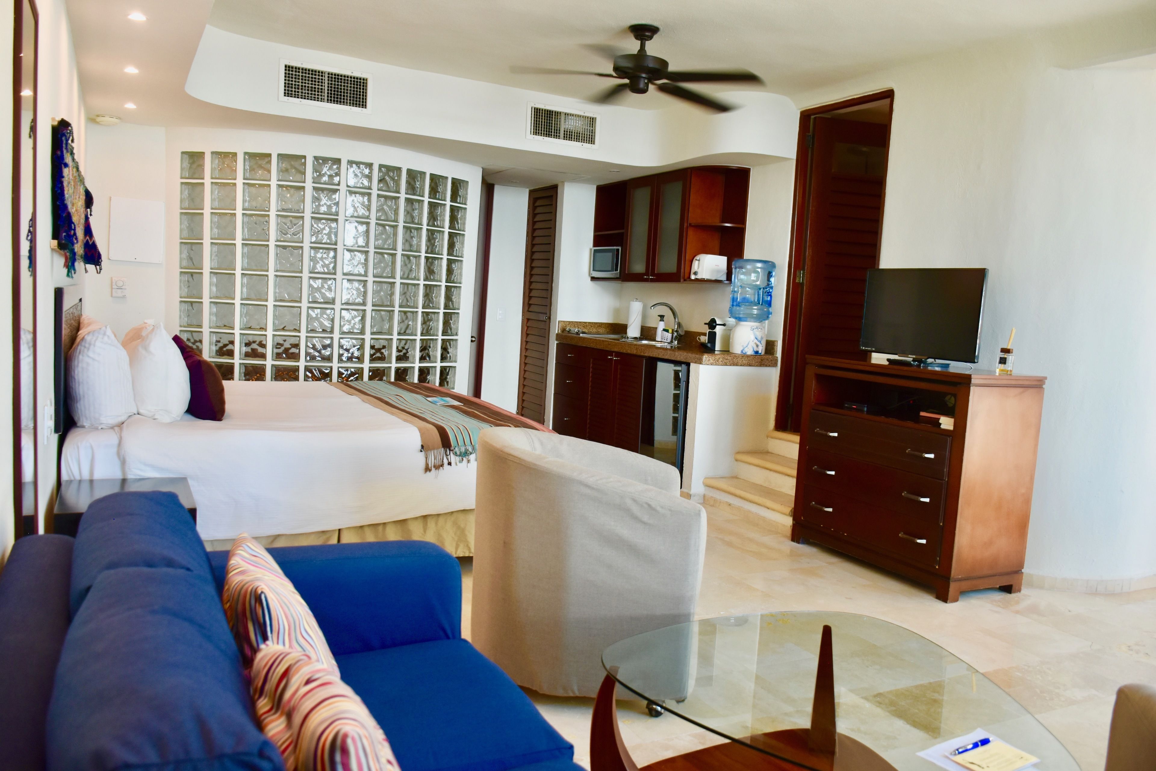 Une chambre d’hôtel moderne équipée d’un lit, d’un canapé bleu, d’une table en verre, d’une kitchenette et d’un téléviseur.