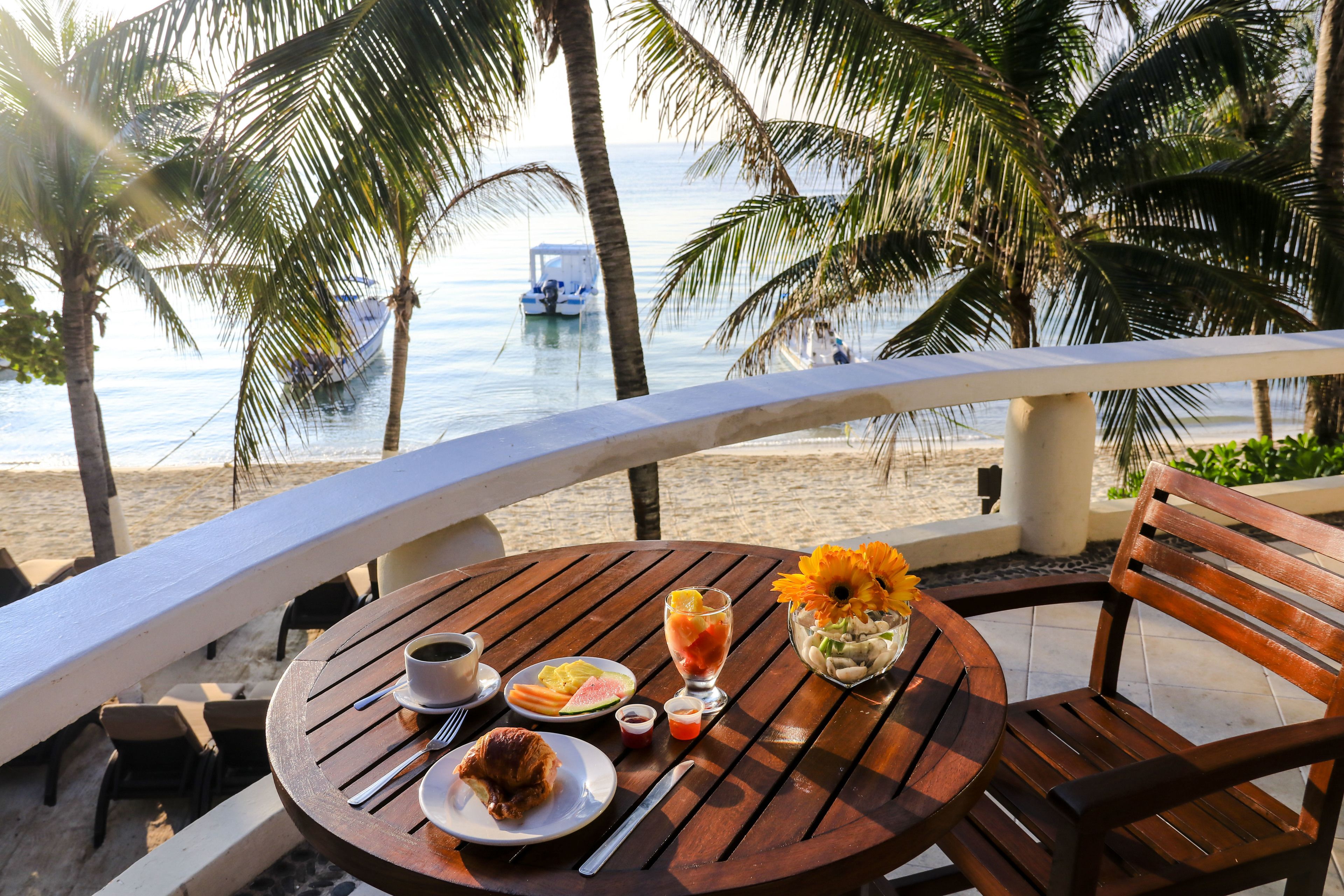 A wooden table with breakfast items, a chair, and a view of the beach and ocean.
