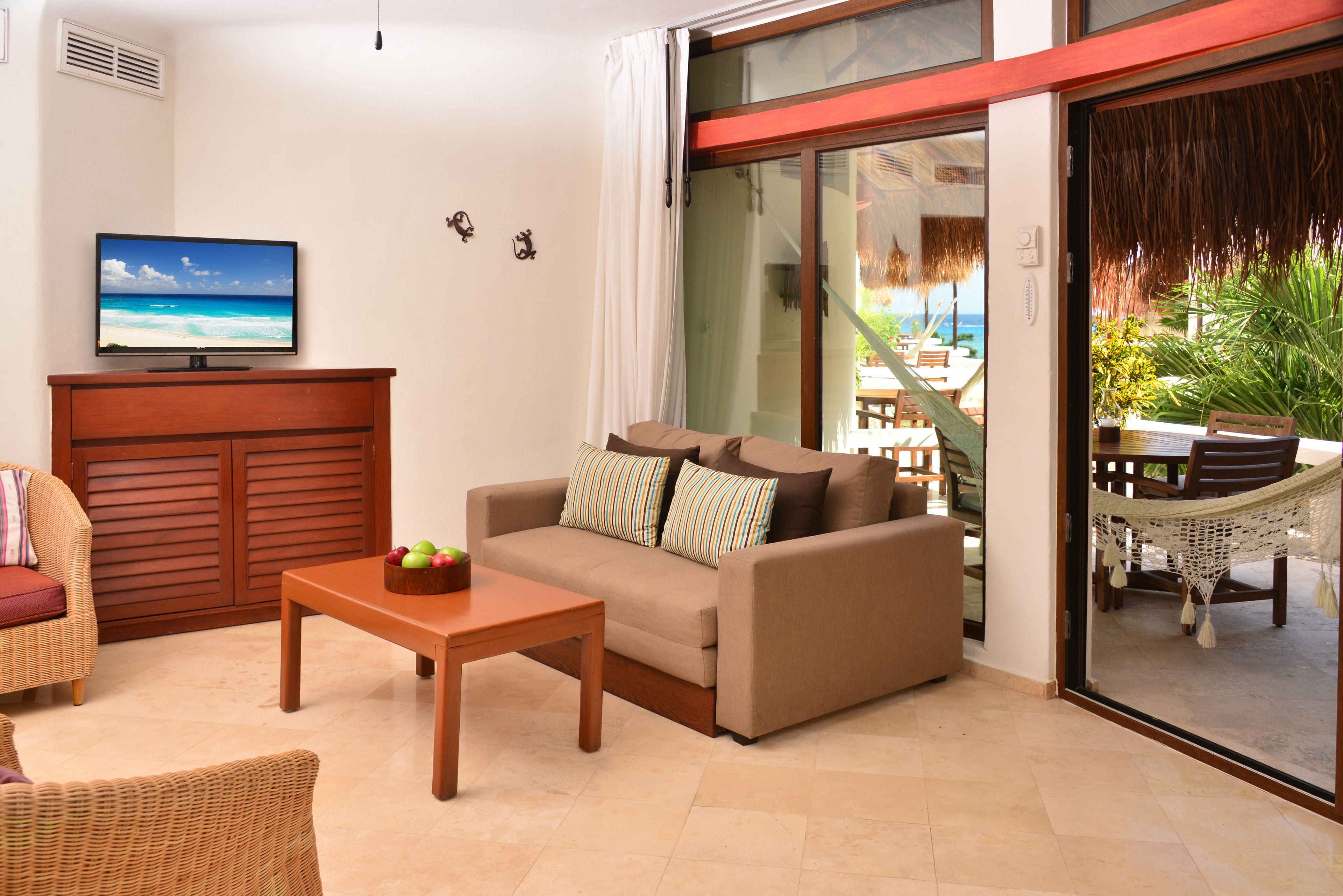 A living room with a sofa, a coffee table, a TV, and a view of the beach through a sliding glass door.