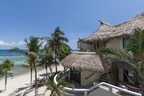 Una proprietà fronte spiaggia con un edificio a tetto di paglia, palme e vista sull'oceano.