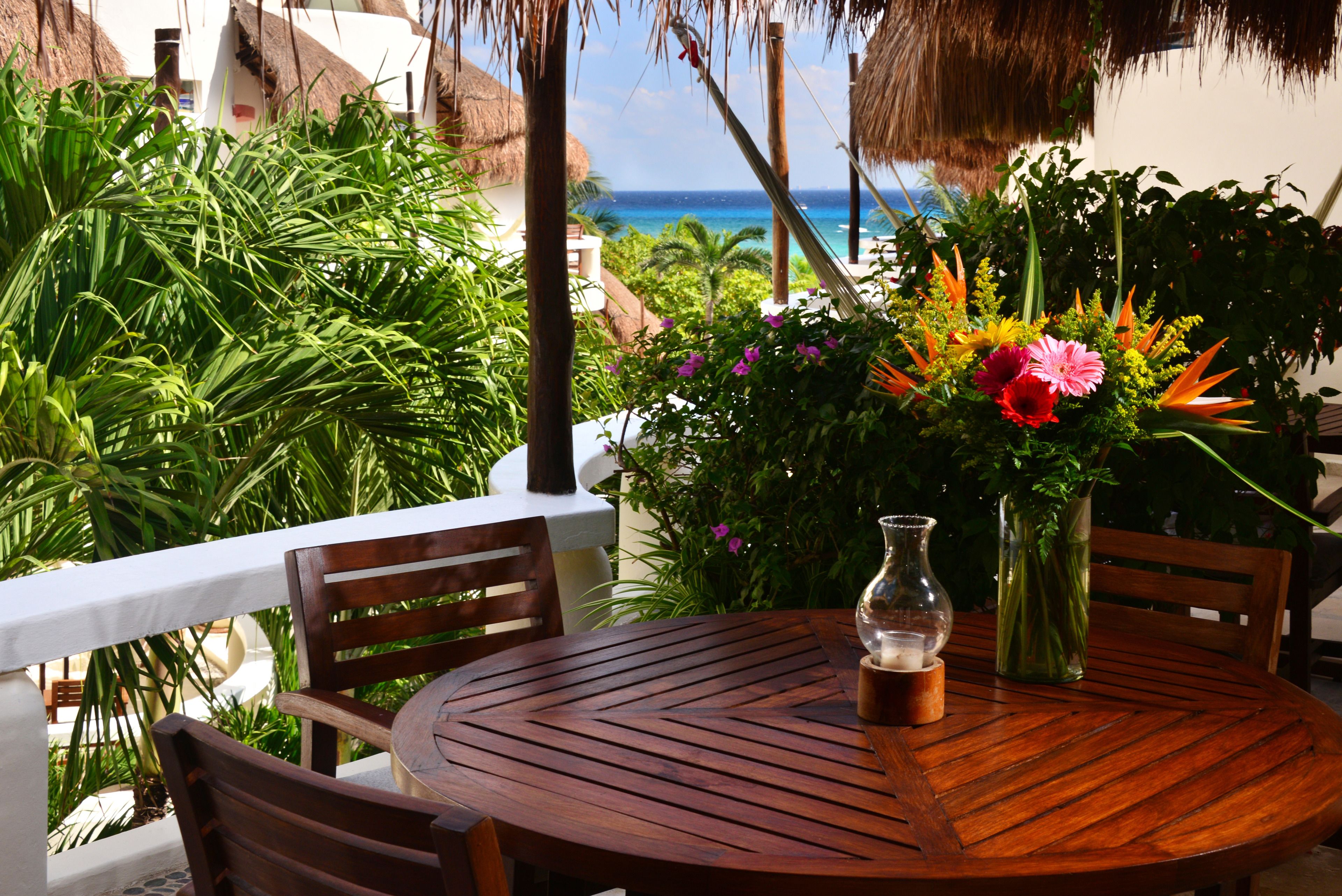 A wooden table with chairs, a vase with flowers, and a view of the ocean.