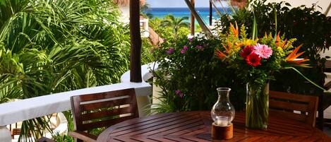 A wooden table with chairs, a vase with flowers, and a view of the ocean.