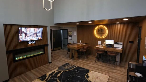 Un hall d’hôtel moderne avec un téléviseur, des panneaux de bois, un luminaire rond et un comptoir d’accueil.