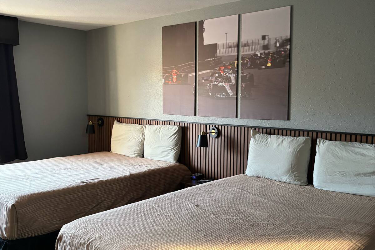 A hotel room with two beds, a large wall-mounted TV displaying a racing event, and a simple, functional design.