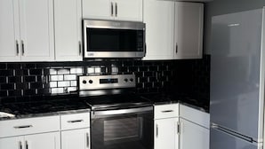 Une cuisine moderne avec des meubles blancs, un dosseret en carreaux noirs, des appareils en acier inoxydable et un plancher en bois.