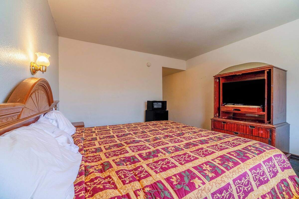 A hotel room with a large bed, a wooden headboard, a television, and a wooden cabinet.