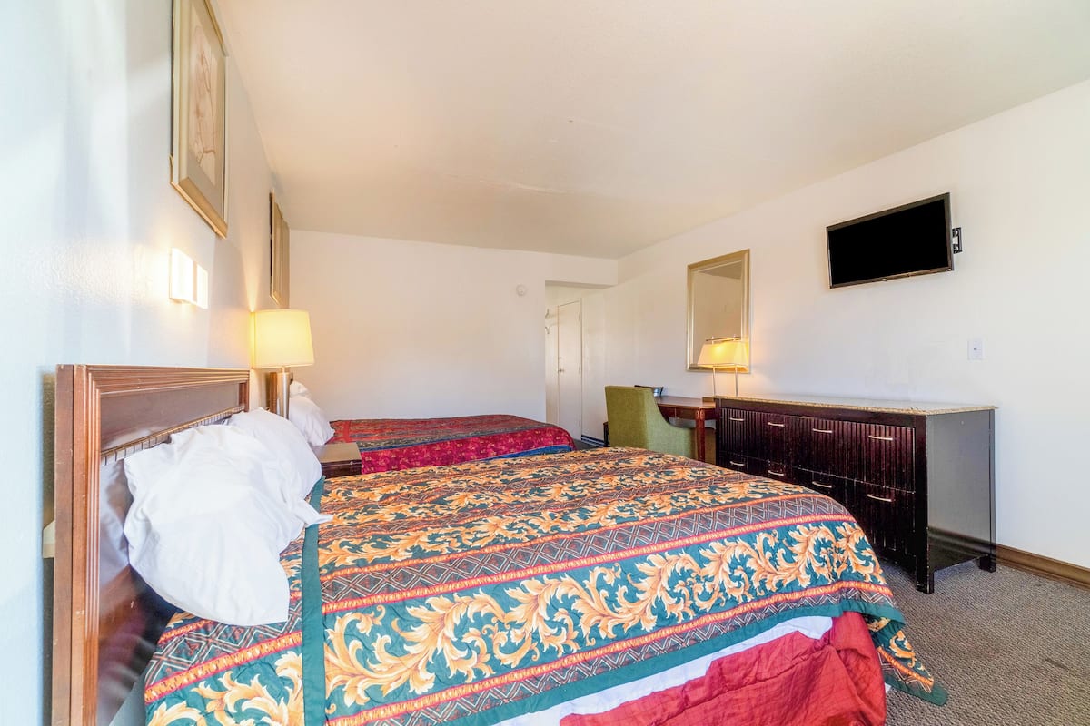 A hotel room with two beds, a desk, a chair, and a television on the wall.