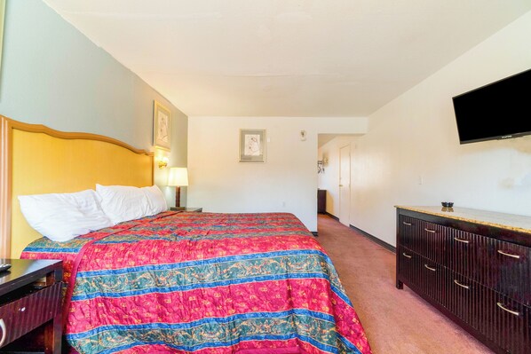 Una habitación de hotel con una cama grande, un aparador, un televisor montado en la pared y un cuadro enmarcado.