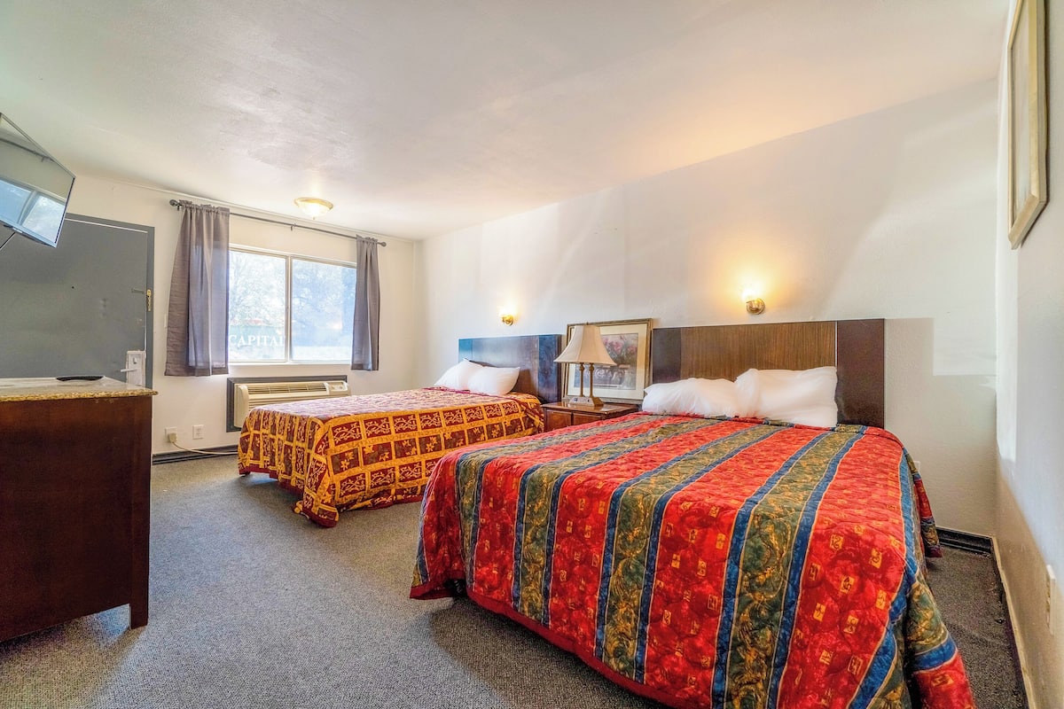 A hotel room with two beds, a desk, and a window with curtains.