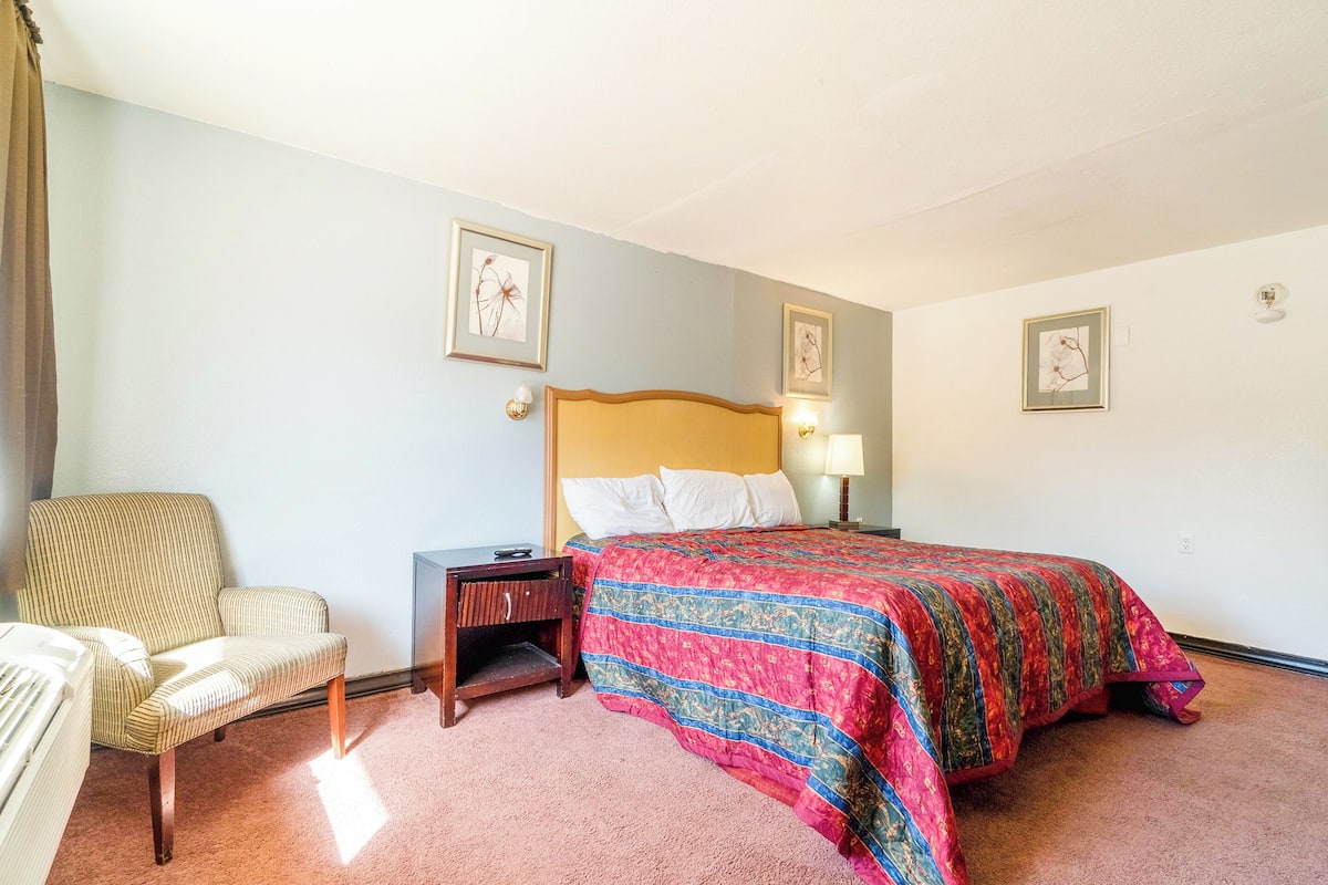 A hotel room with a bed, a chair, a nightstand, and two wall-mounted lamps.
