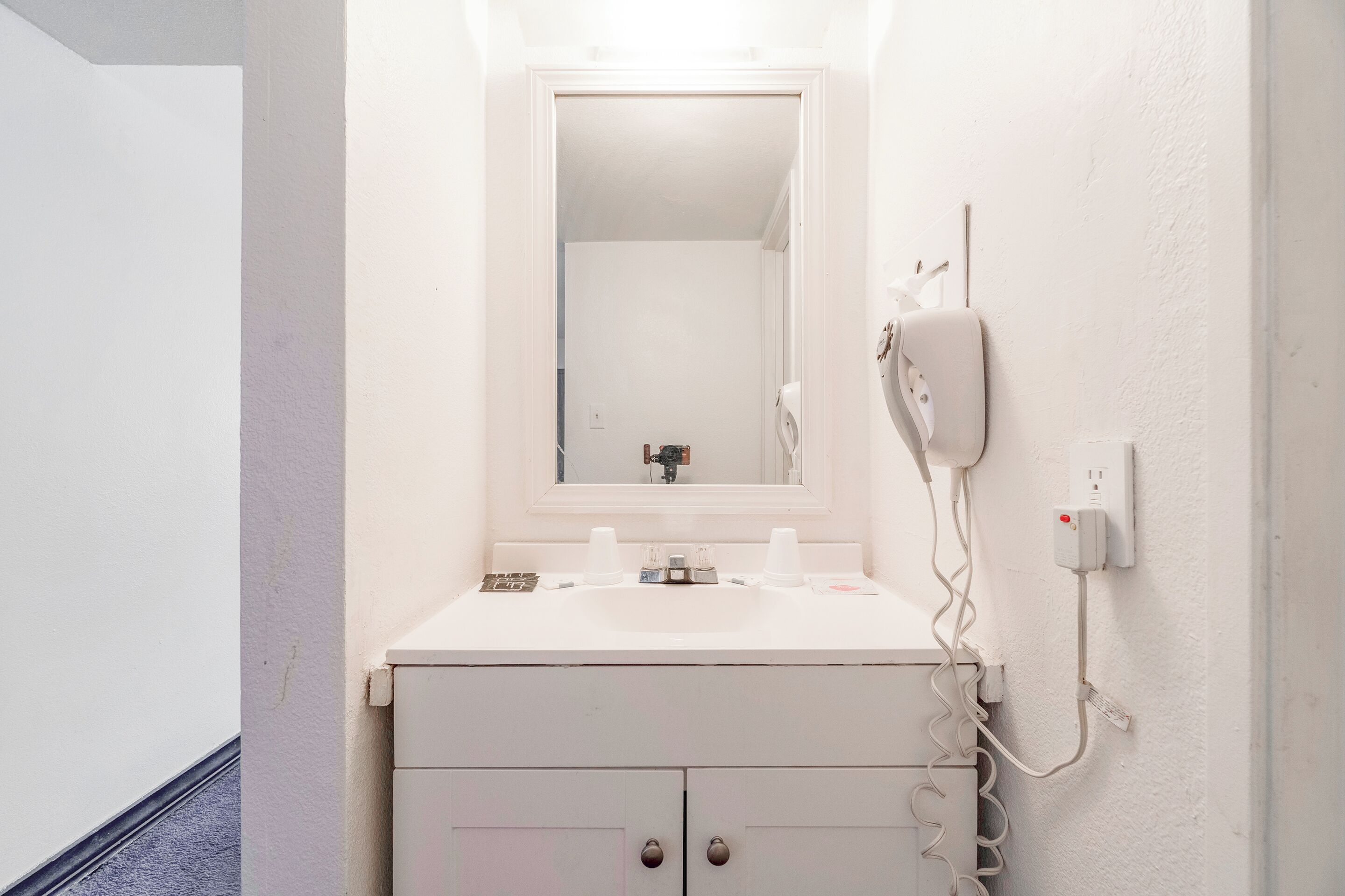 Une salle de bain avec un lavabo blanc, un miroir et un sèche-cheveux fixé au mur.