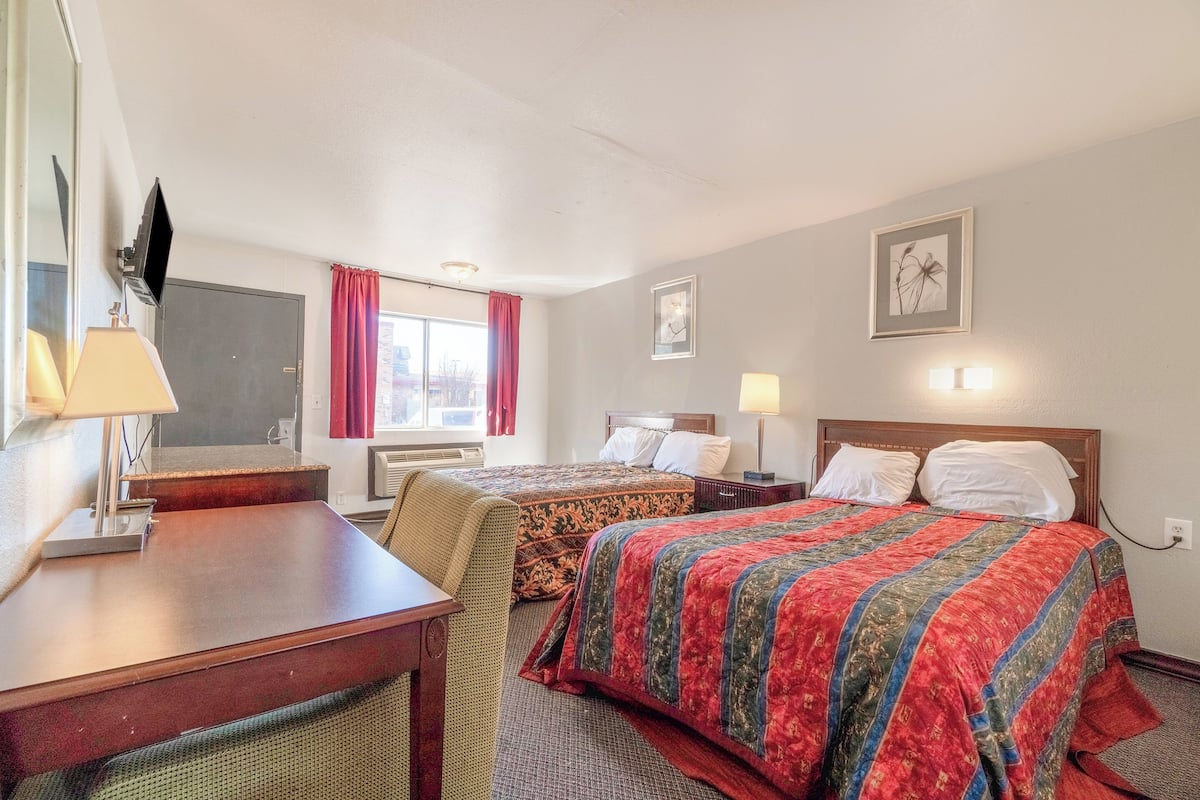 A hotel room with two beds, a desk, a TV, and a window with curtains.