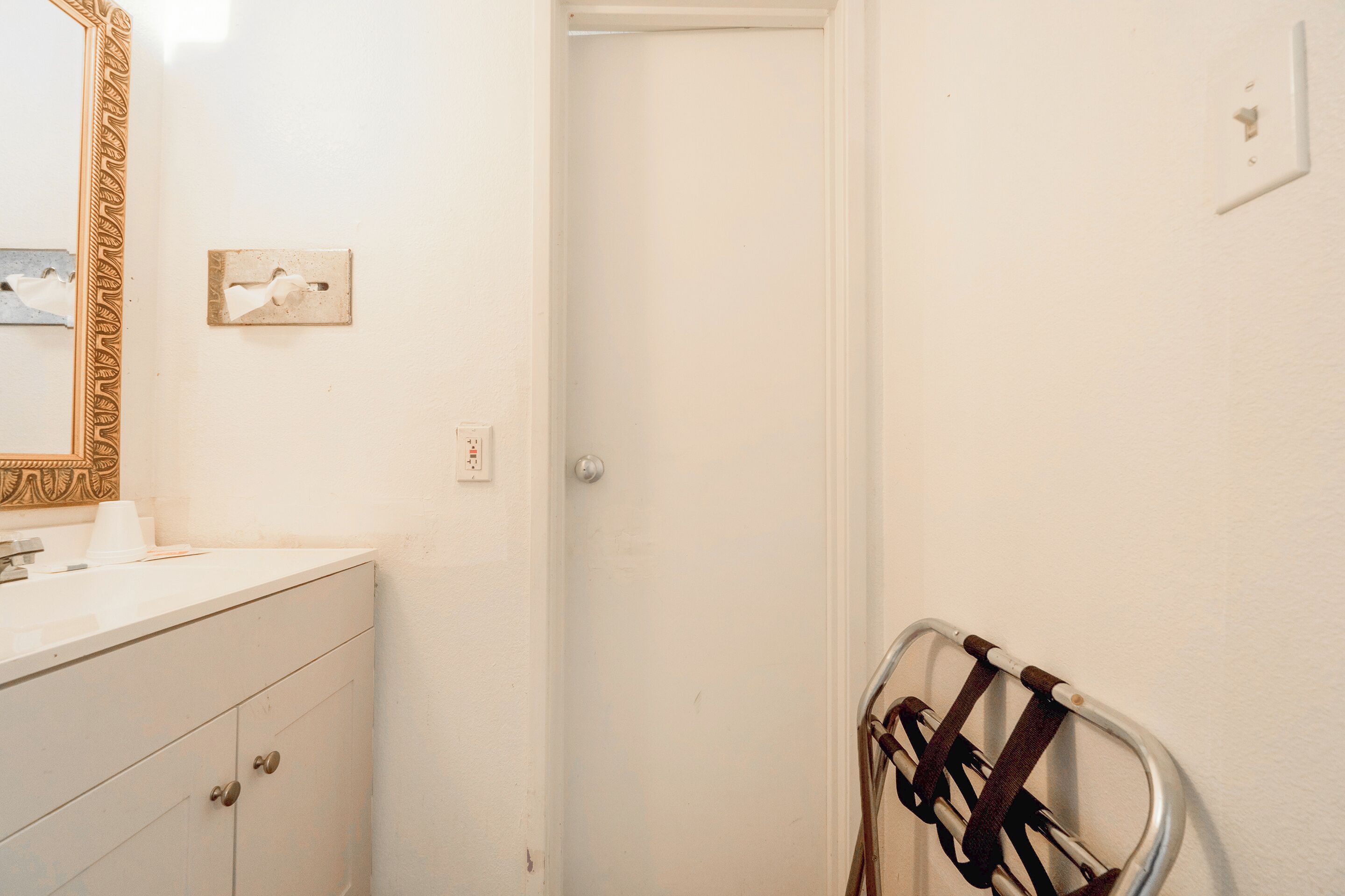 A bathroom with a white vanity, a mirror with a decorative frame, a towel rack, and a door.