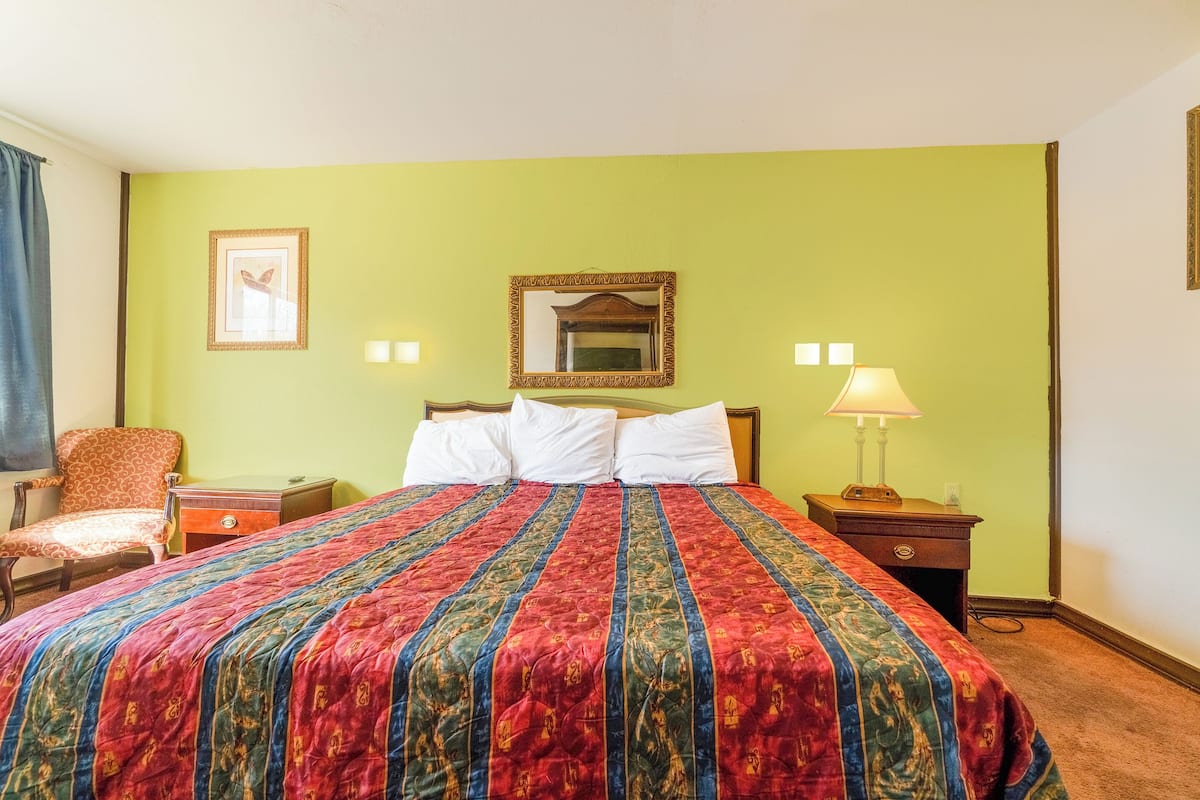 A hotel room with a large bed, a chair, a nightstand, and a lamp.