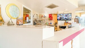 Een hotel receptie met een grote klok, een metalen rek en meerdere schermen aan de muur.
