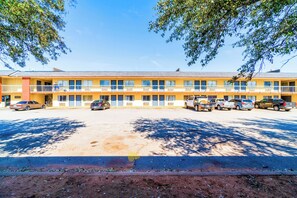 A motel with a row of rooms, a parking lot, and a clear sky.