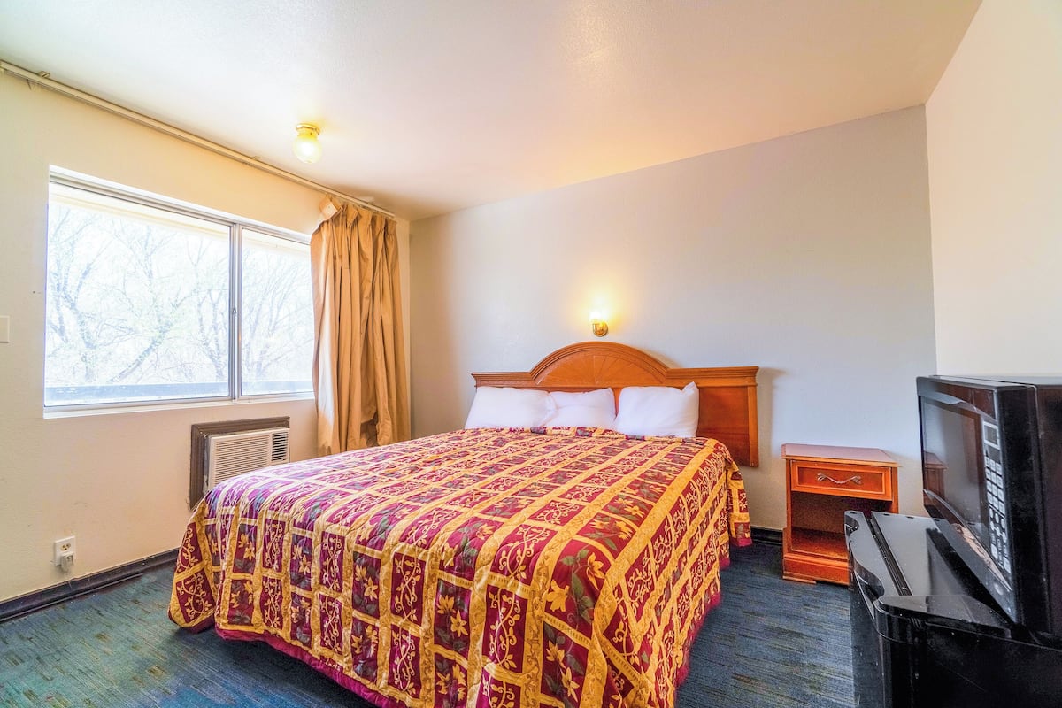 A hotel room with a large bed, a wooden headboard, a television, and a window with curtains.