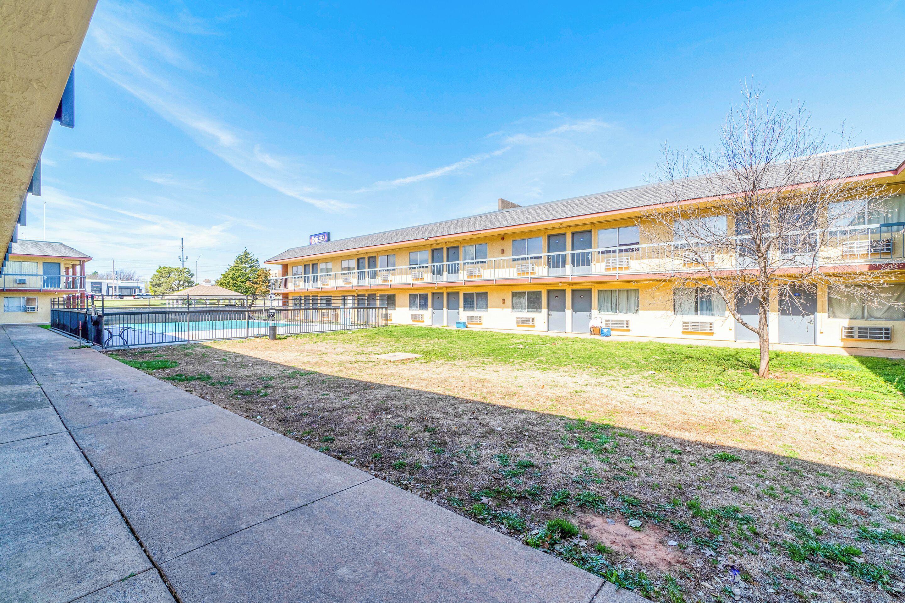 A multi-story motel with a flat roof, a fenced courtyard, and a clear blue sky.