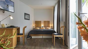 A modern bedroom with a bed, two chairs, a desk, and a TV on the wall.