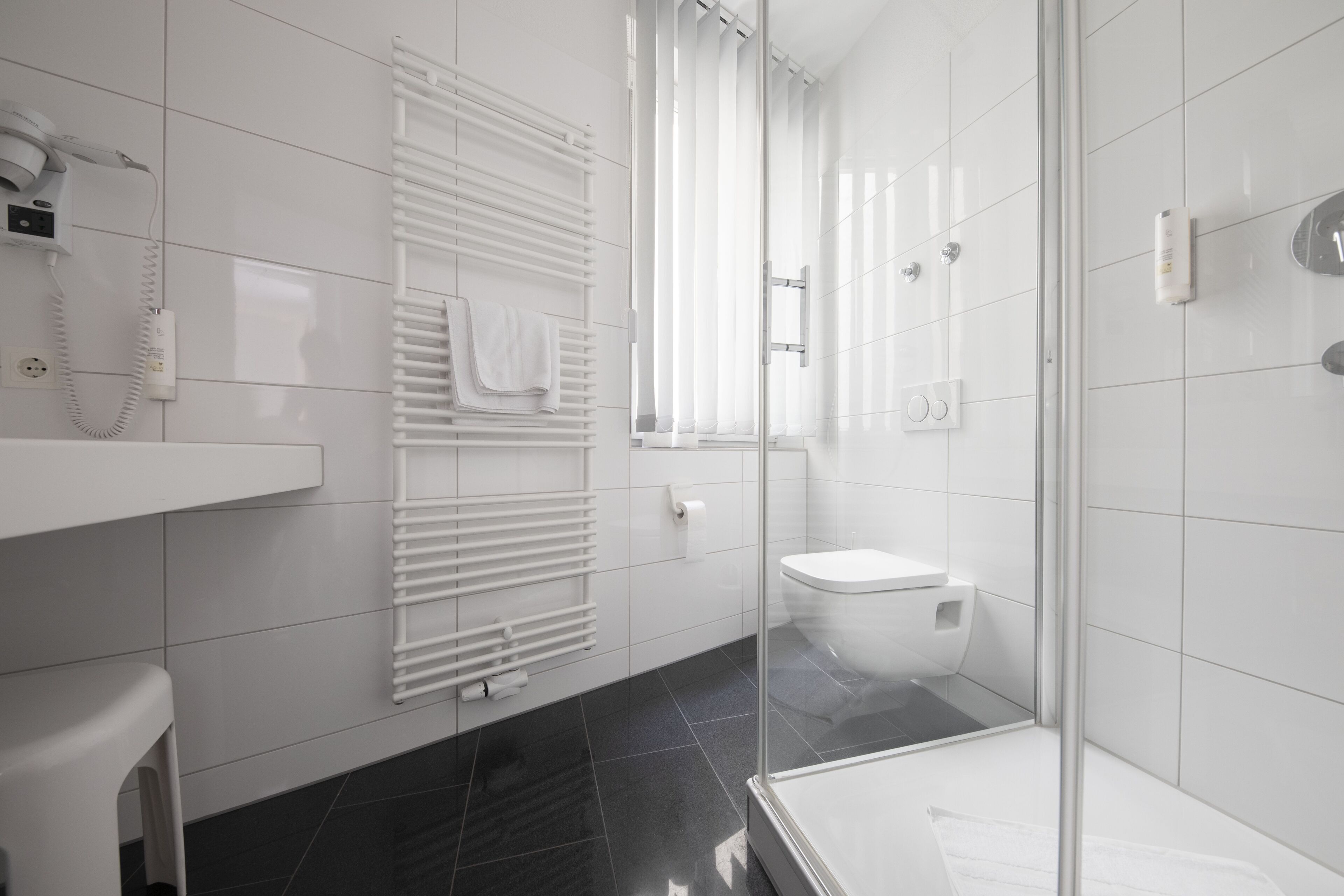 Un baño moderno con cabina de ducha de vidrio, inodoro blanco y perchero para toallas.